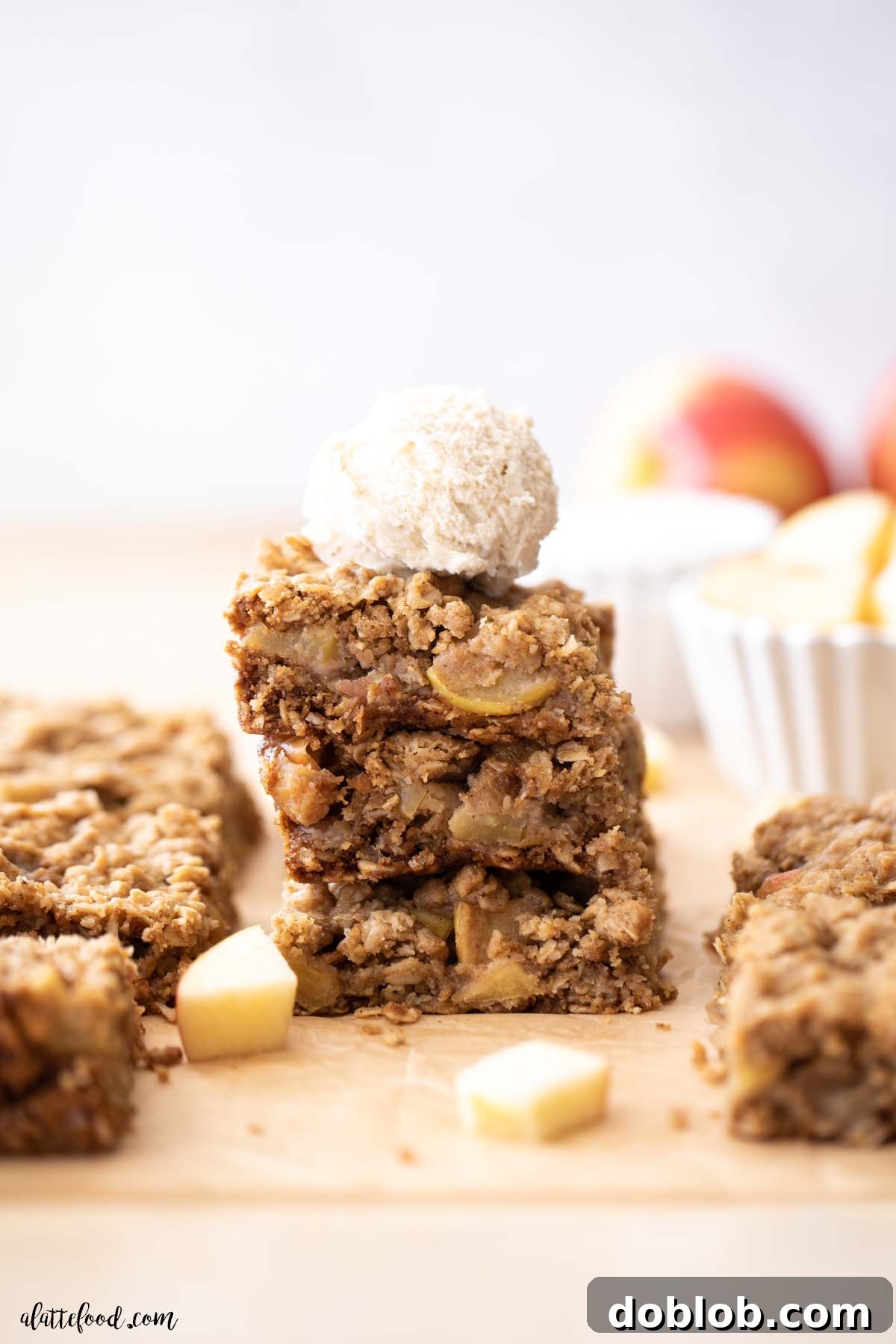 stack of caramel apple bars with oatmeal topping on brown parchment paper with a scoop of ice cream on top.