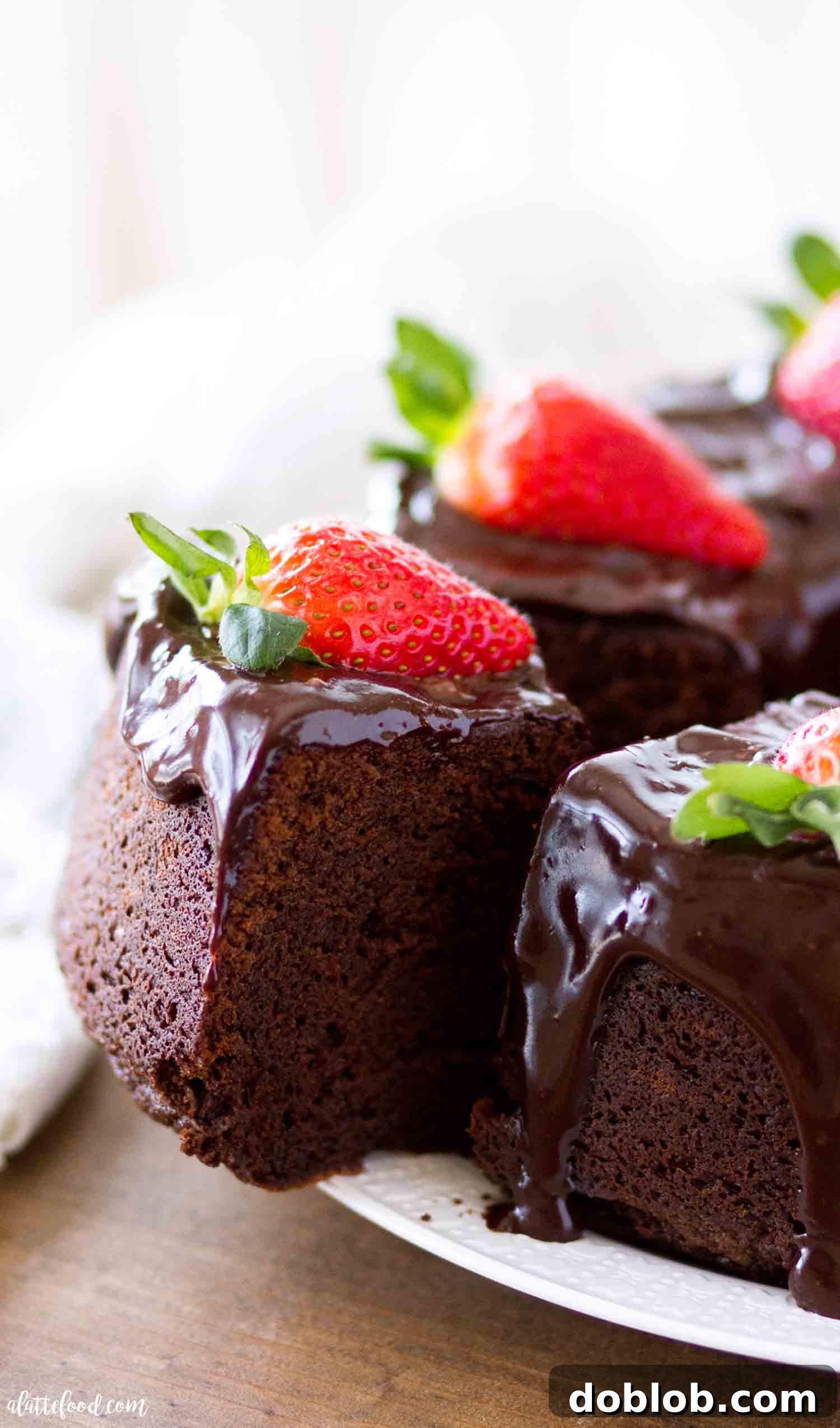 The best chocolate pound cake, made with melted chocolate instead of cocoa powder, boasts a rich, fudgy texture. Topped with ganache and fresh strawberries, it's a truly delightful chocolate dessert! A delectable slice of chocolate pound cake with rich ganache, garnished with fresh strawberries, resting on a pristine white plate, showcasing its moist texture.