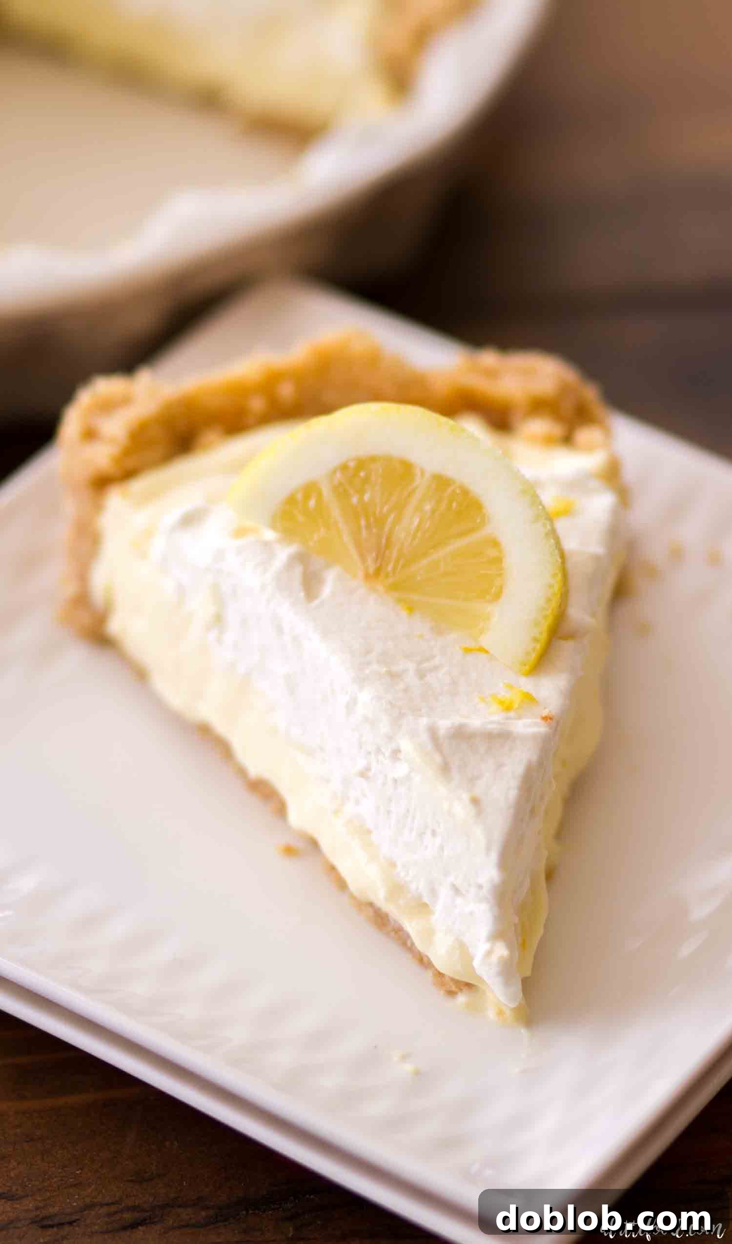 Slice of No-Bake Lemon Cream Pie with Lemon Whipped Cream on a Golden Oreo Vanilla Wafer Crust. A perfect slice of No-Bake Lemon Cream Pie, showcasing its creamy texture, topped with a swirl of homemade lemon whipped cream, and resting on its distinct vanilla wafer and Golden Oreo crust.