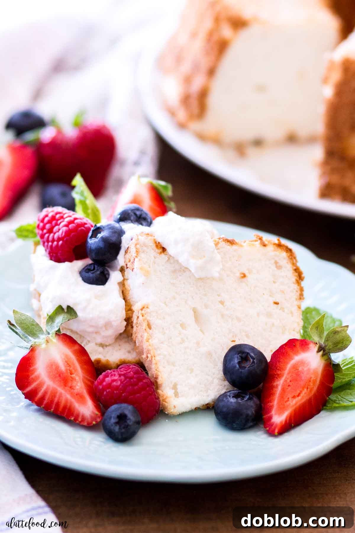 homemade angel food cake slice with fresh berries and whipped cream on blue plate.