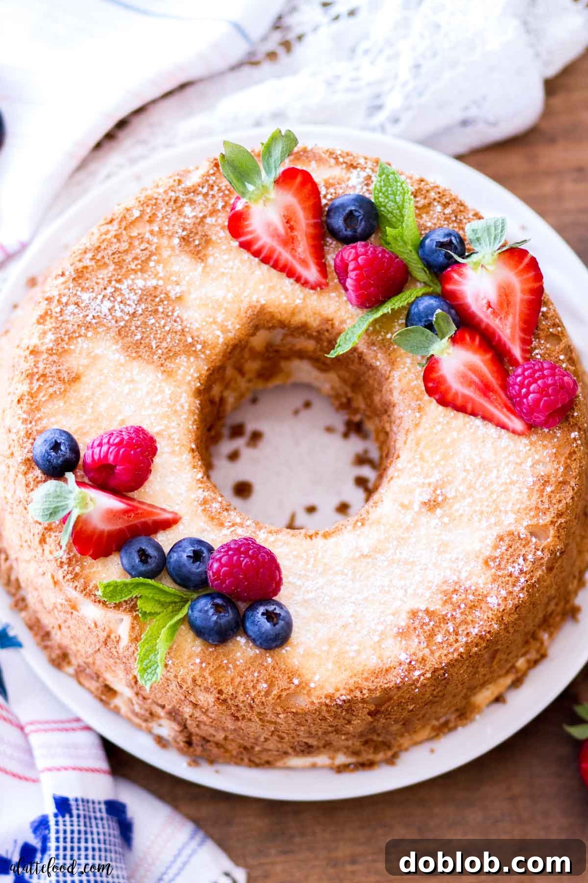 homemade angel food cake topped with fresh berries and mint on a white plate.