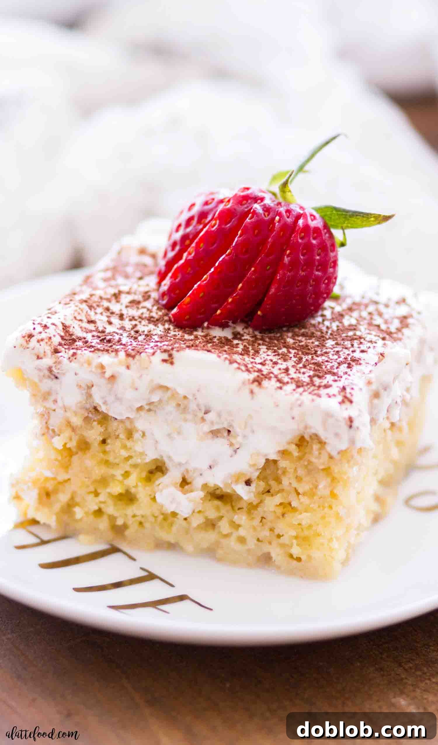This tiramisu poke cake is soaked with a coffee cream, topped with whipped cream frosting, and each slice is served on a white plate with fresh strawberries.