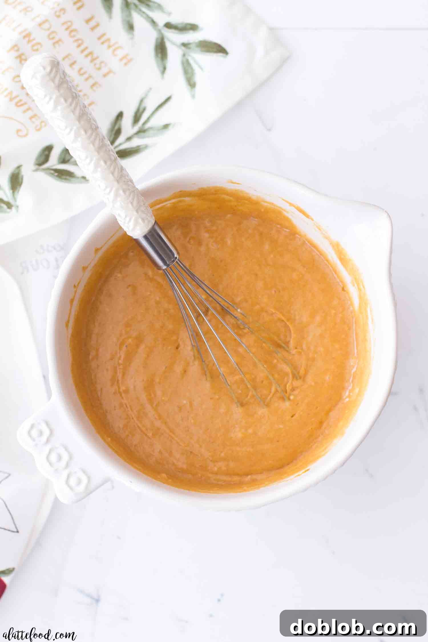 Pumpkin poke cake batter in a white mixing bowl, showcasing its smooth, spiced orange hue.