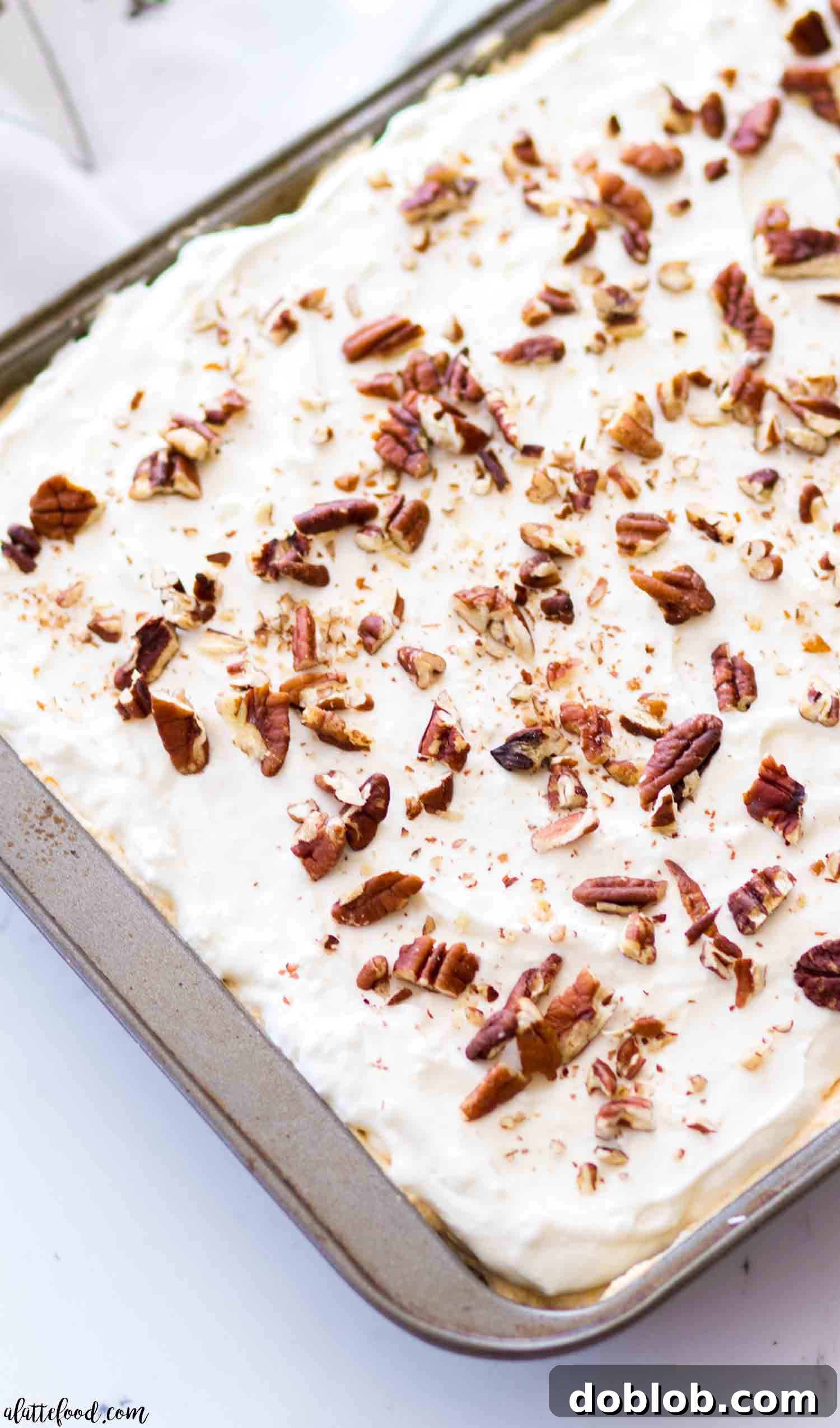 A full Pumpkin Pie Poke Cake in a baking pan, topped with cream cheese frosting and pecans, ready for chilling and serving.
