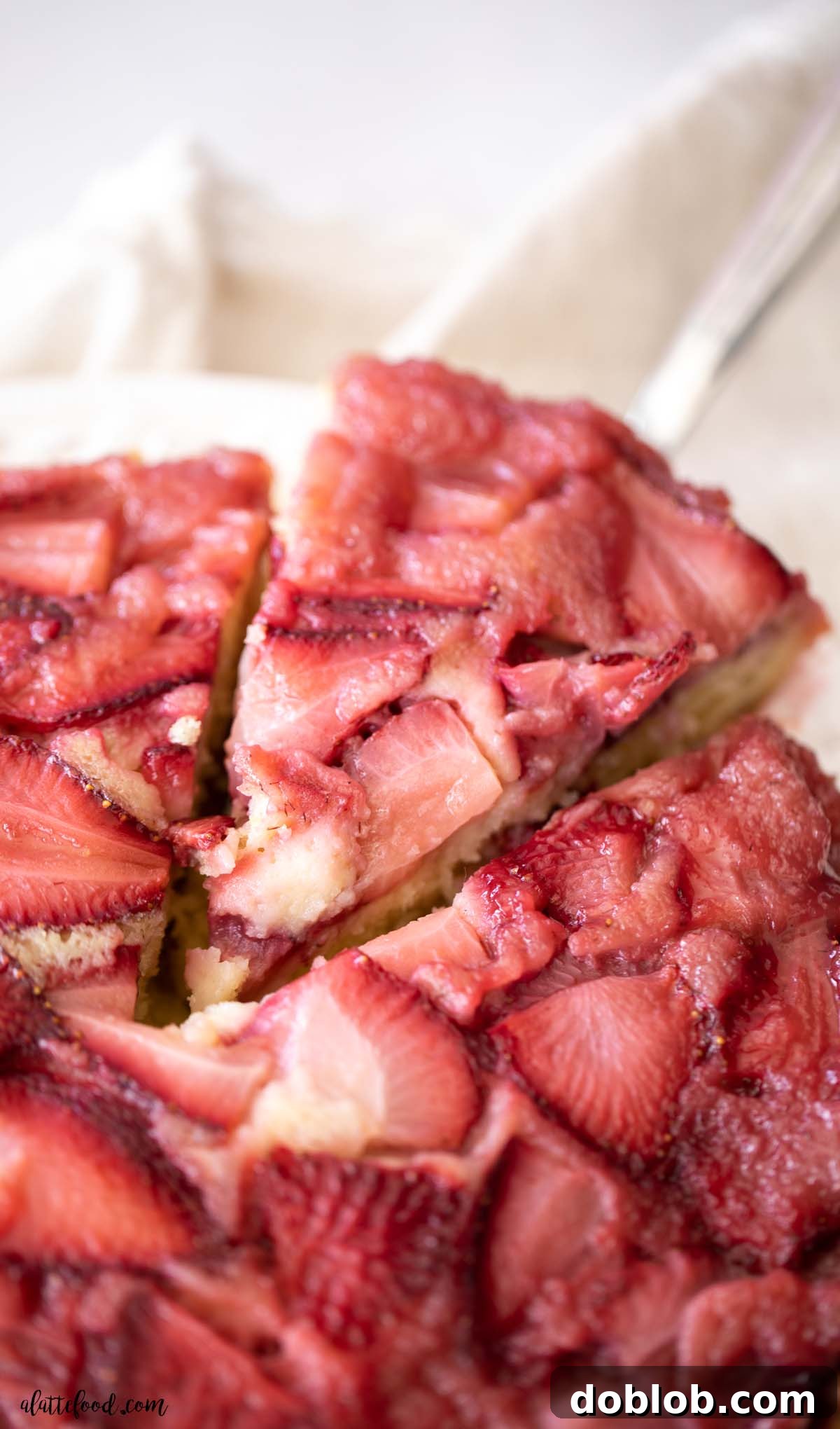 A slice of baked strawberry upside down cake on a silver cake server, showing the vibrant strawberry topping and fluffy cake base.