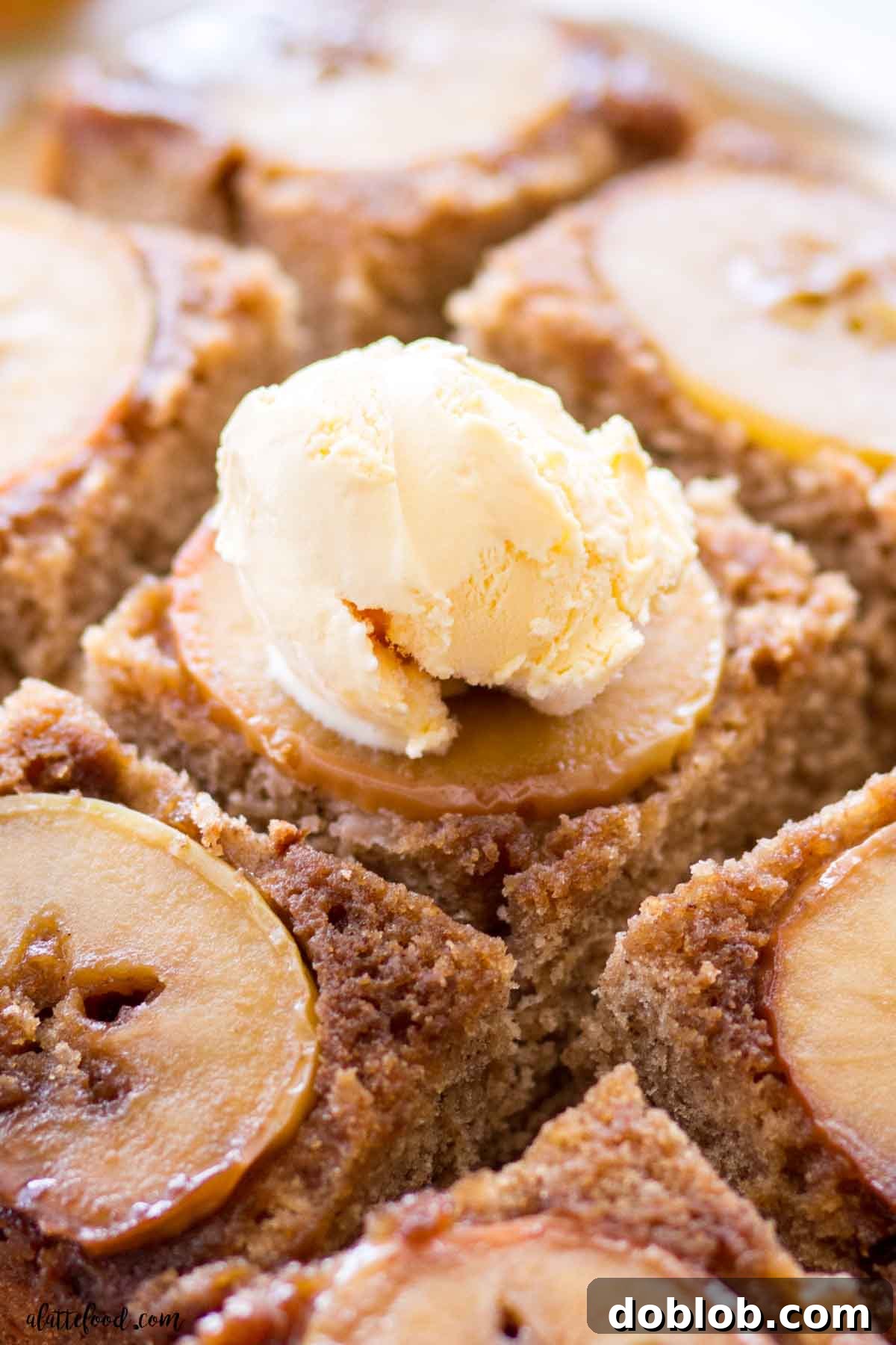 A tempting slice of Caramel Apple Upside Down Cake, elegantly presented with a scoop of creamy vanilla ice cream melting on top, highlighting the luscious caramel sauce.