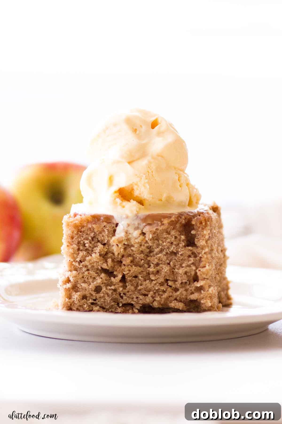 A beautifully presented Apple Upside Down Cake, topped with a generous scoop of melting vanilla ice cream and drizzled with glistening caramel sauce on a pristine white plate.