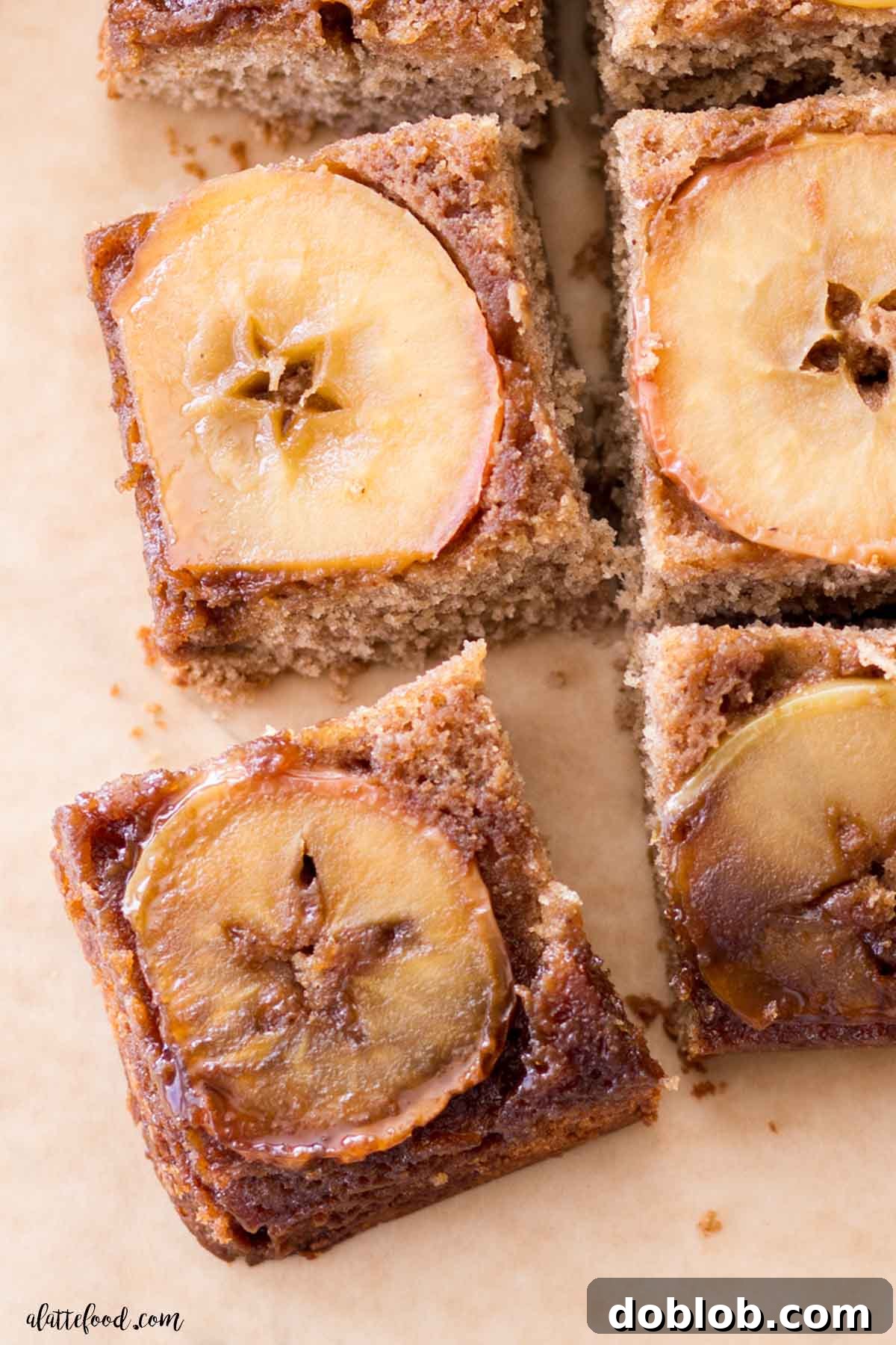 A close-up of a freshly baked Apple Upside Down Cake, beautifully cut into individual slices and arranged on brown parchment paper, showcasing the golden caramel and soft apple layer.