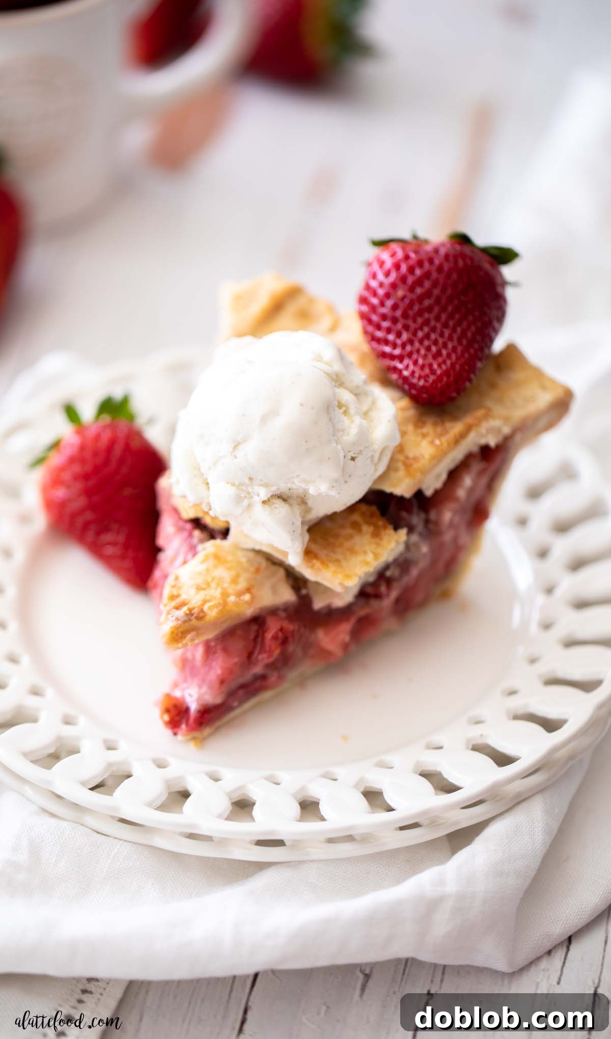 Vanilla ice cream-topped strawberry pie served on a white beveled plate with fresh strawberries on the side.