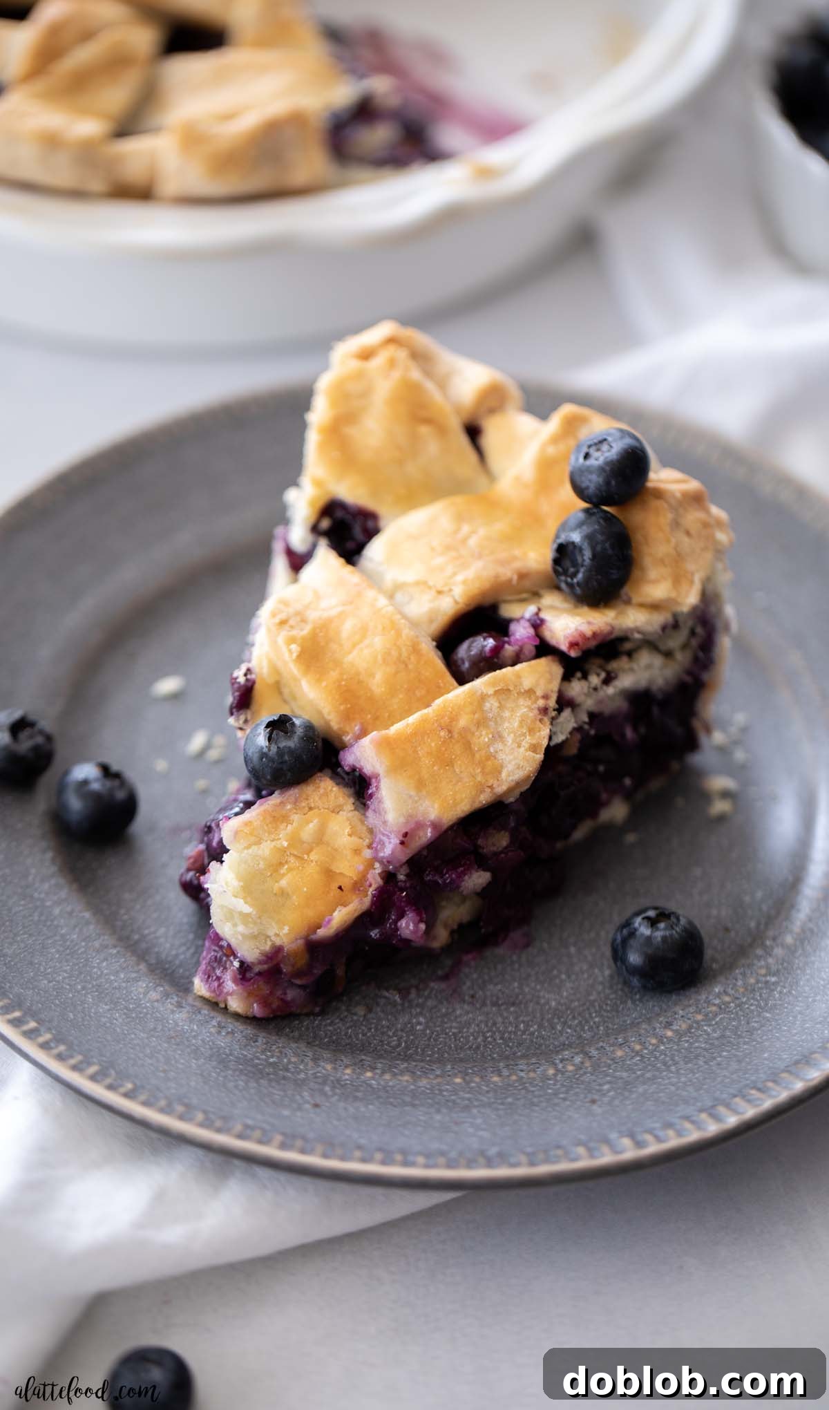 A slice of fresh blueberry pie with a lattice crust on a gray plate, highlighting its vibrant filling and flaky pastry.