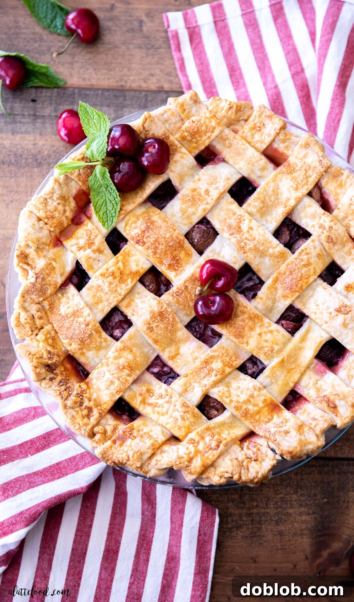 A beautifully crafted lattice-crusted cherry pie, baked in a glass dish and cooling on a striped kitchen towel, showcasing its golden-brown perfection.