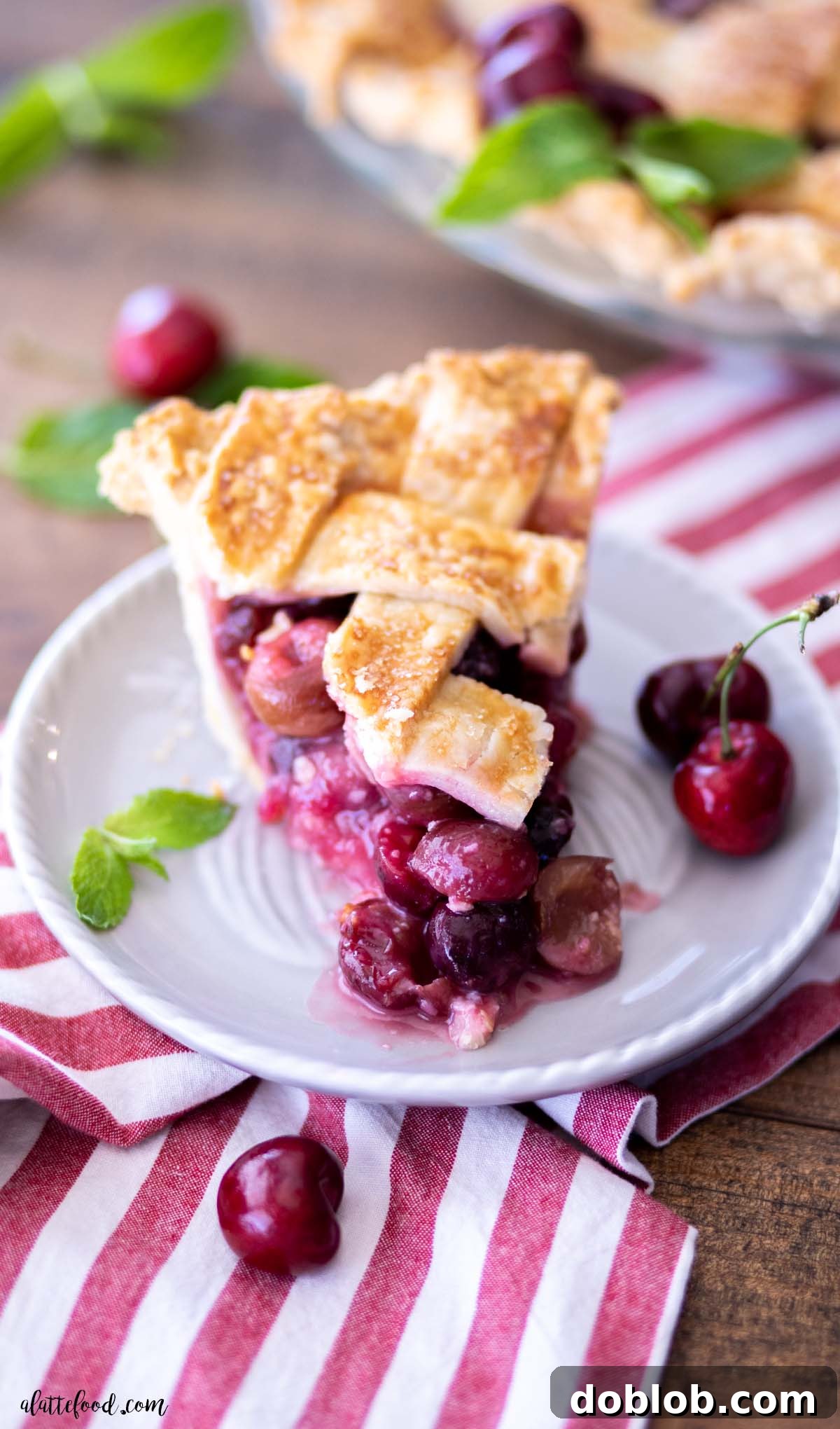 A close-up of a flaky cherry pie slice featuring a delicate lattice crust, resting on a striped towel, highlighting its handcrafted appeal.