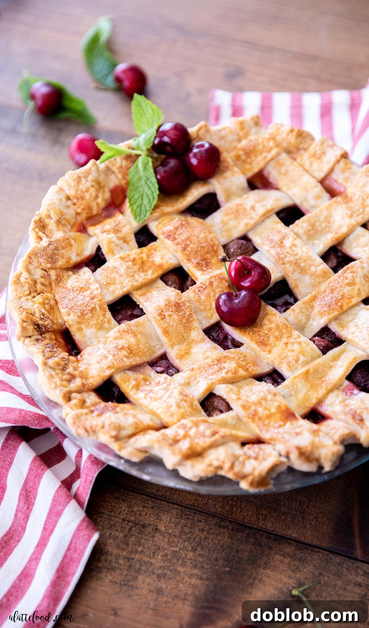 A beautifully baked whole sweet cherry pie with a golden-brown lattice crust, resting on a red striped towel, showcasing its rustic charm.