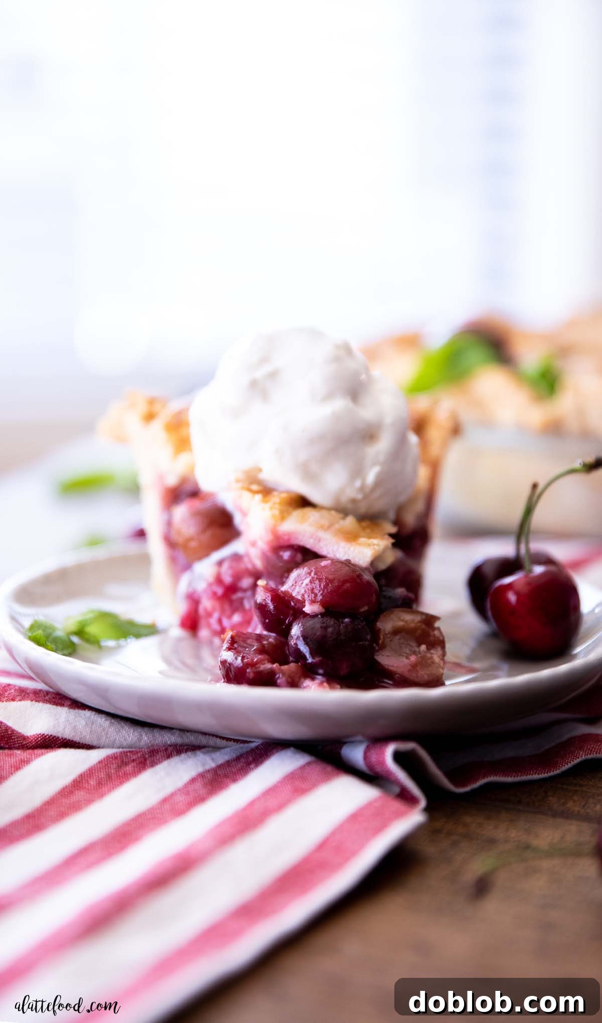 A generous slice of sweet cherry pie, topped with a melting scoop of vanilla ice cream, served on a gray plate, ready to be enjoyed.