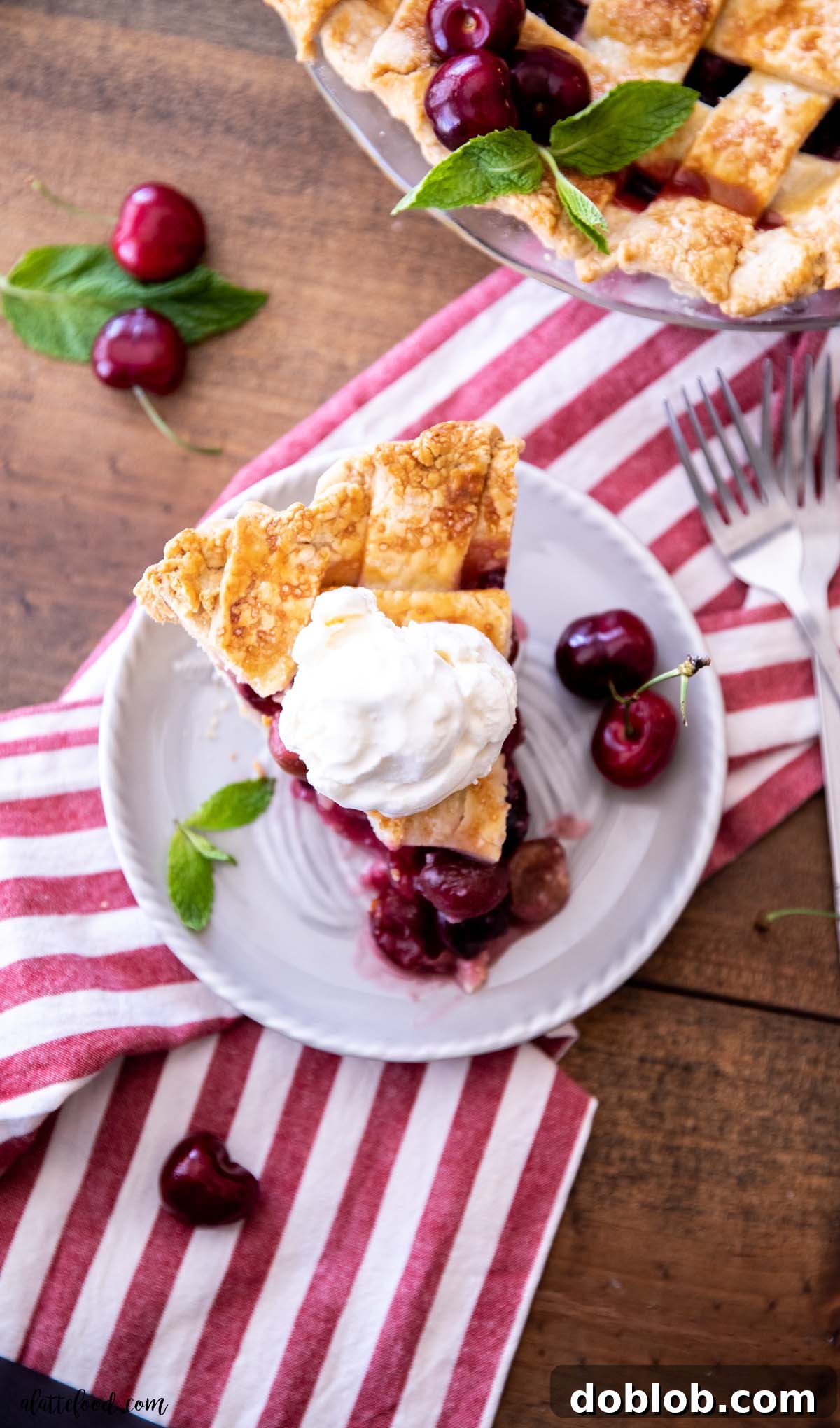 A delectable slice of fresh cherry pie topped with a generous scoop of vanilla ice cream, presented on a red striped towel, embodying the perfect summer dessert.