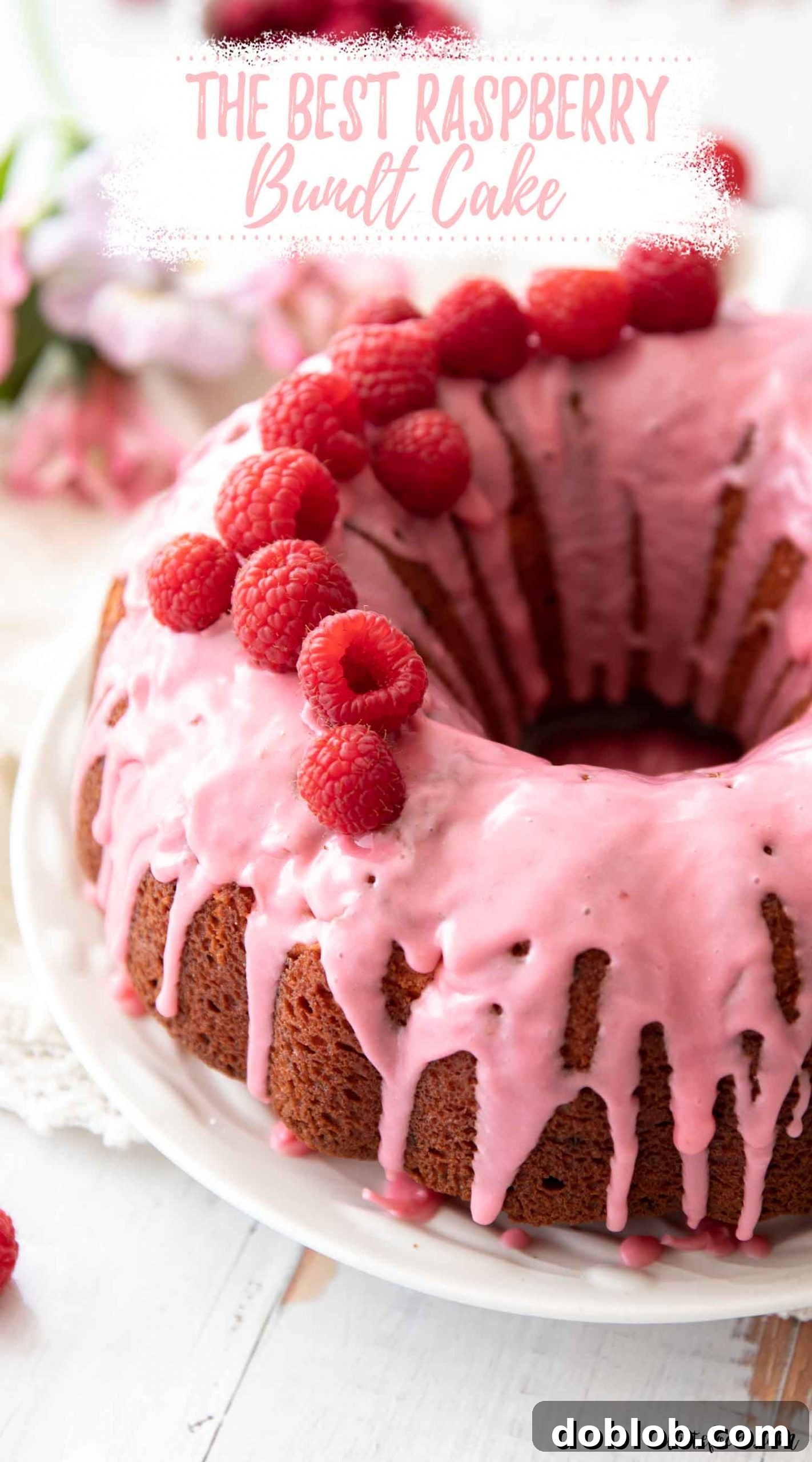 My favorite Raspberry Bundt Cake Recipe, made entirely from scratch with fresh and freeze-dried raspberries, is a light and fluffy sour cream bundt cake—almost like a raspberry pound cake. It’s an easy baking recipe, perfect for Valentine’s Day! A fresh raspberry bundt cake adorned with a delicate raspberry glaze, displayed on a pristine white-washed wooden board.