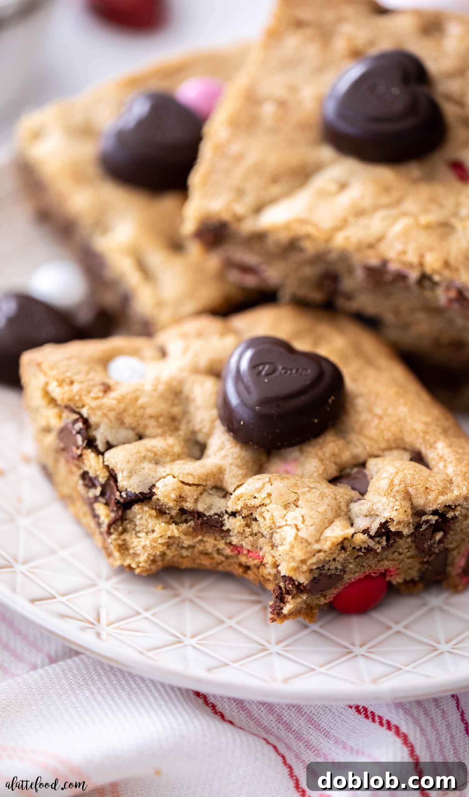 Luscious Raspberry Bundt Cake 3 A delicious chocolate chip M&M cookie bar with a bite taken out, resting on a cream-colored plate, highlighting its chewy texture and colorful candies.