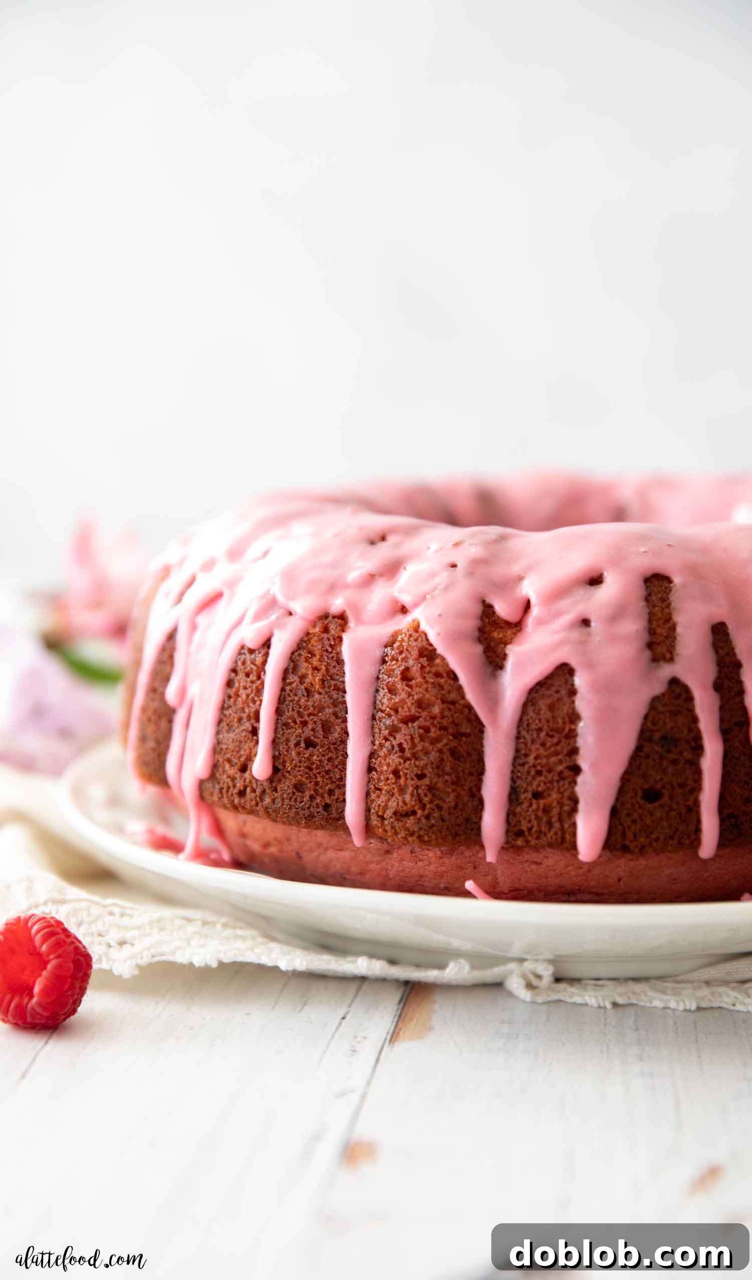 Discover the best Raspberry Bundt Cake recipe made entirely from scratch, free from artificial gelatin or cake mixes. This soft and fluffy cake owes its rich texture to sour cream and simple, wholesome ingredients, making it a beloved family dessert. Close-up view of the rich, pink raspberry glaze elegantly cascading down the sides of a freshly baked bundt cake, highlighting its moist texture.