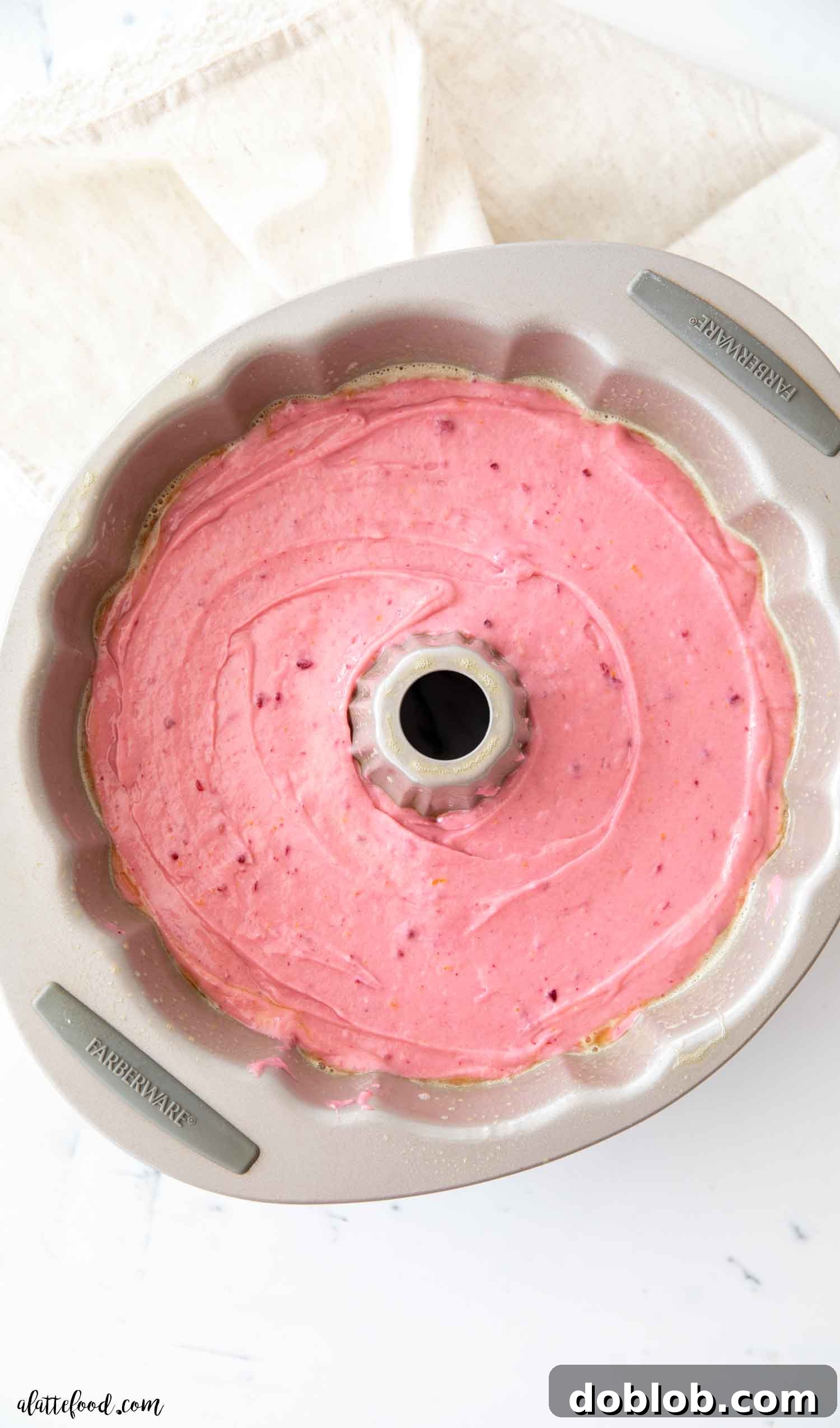 This pretty in pink Raspberry Cake features a fresh raspberry sauce and freeze-dried raspberries, baked as a from-scratch bundt cake (no cake mix or gelatin needed!) with sour cream, orange juice, and almond essence for a truly delightful dessert. Unbaked vibrant pink raspberry cake batter filling a classic silver bundt cake pan, ready for the oven.