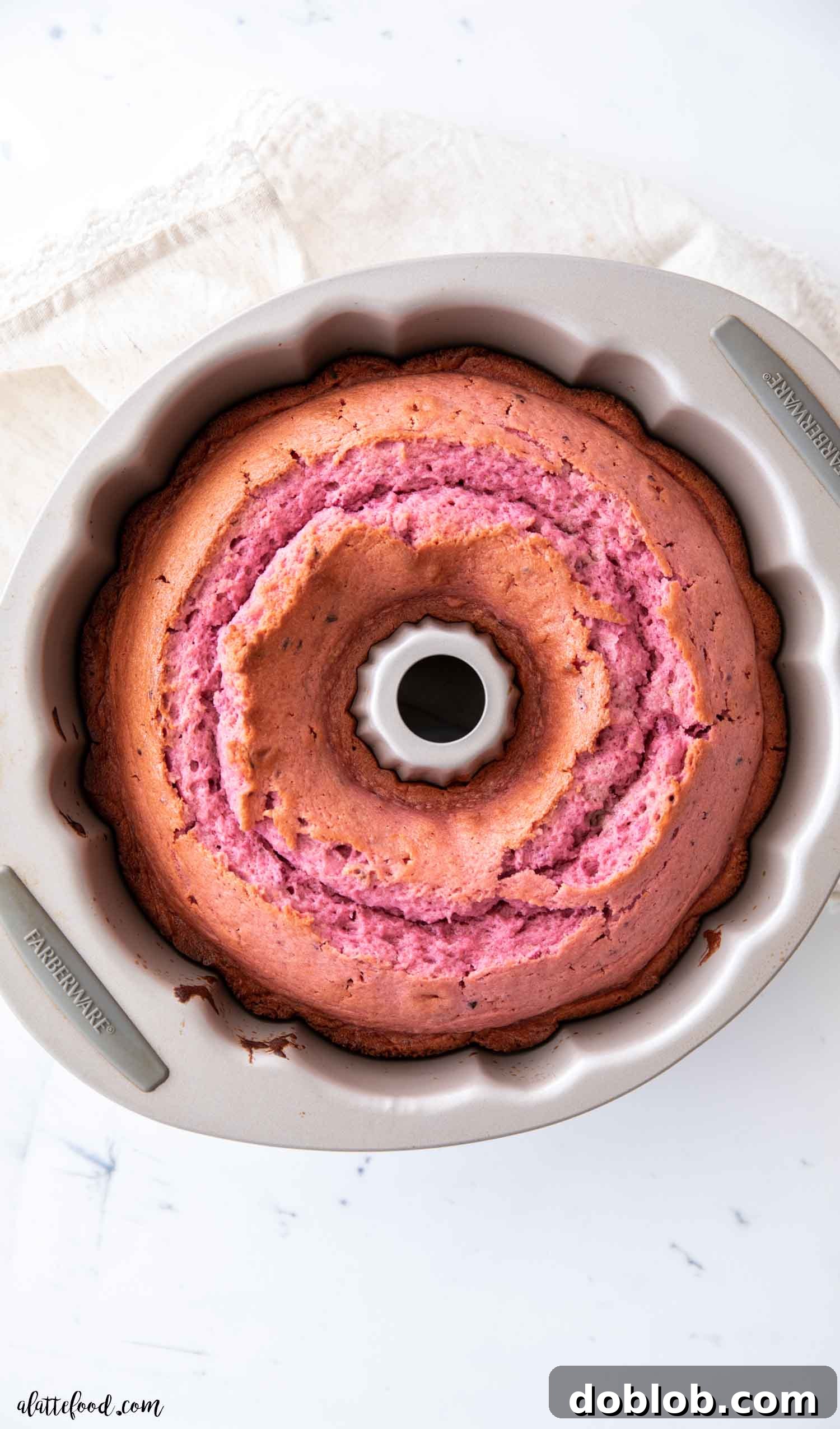 This easy Raspberry Bundt Cake recipe, made with fresh and freeze-dried berries, is 100% from scratch – a raspberry cake without gelatin or cake mix. This light and fluffy sour cream bundt cake is perfect for Valentine's Day or any raspberry dessert lover. A freshly baked raspberry cake, perfectly golden brown, still nestled in its gleaming silver bundt cake pan after cooling.
