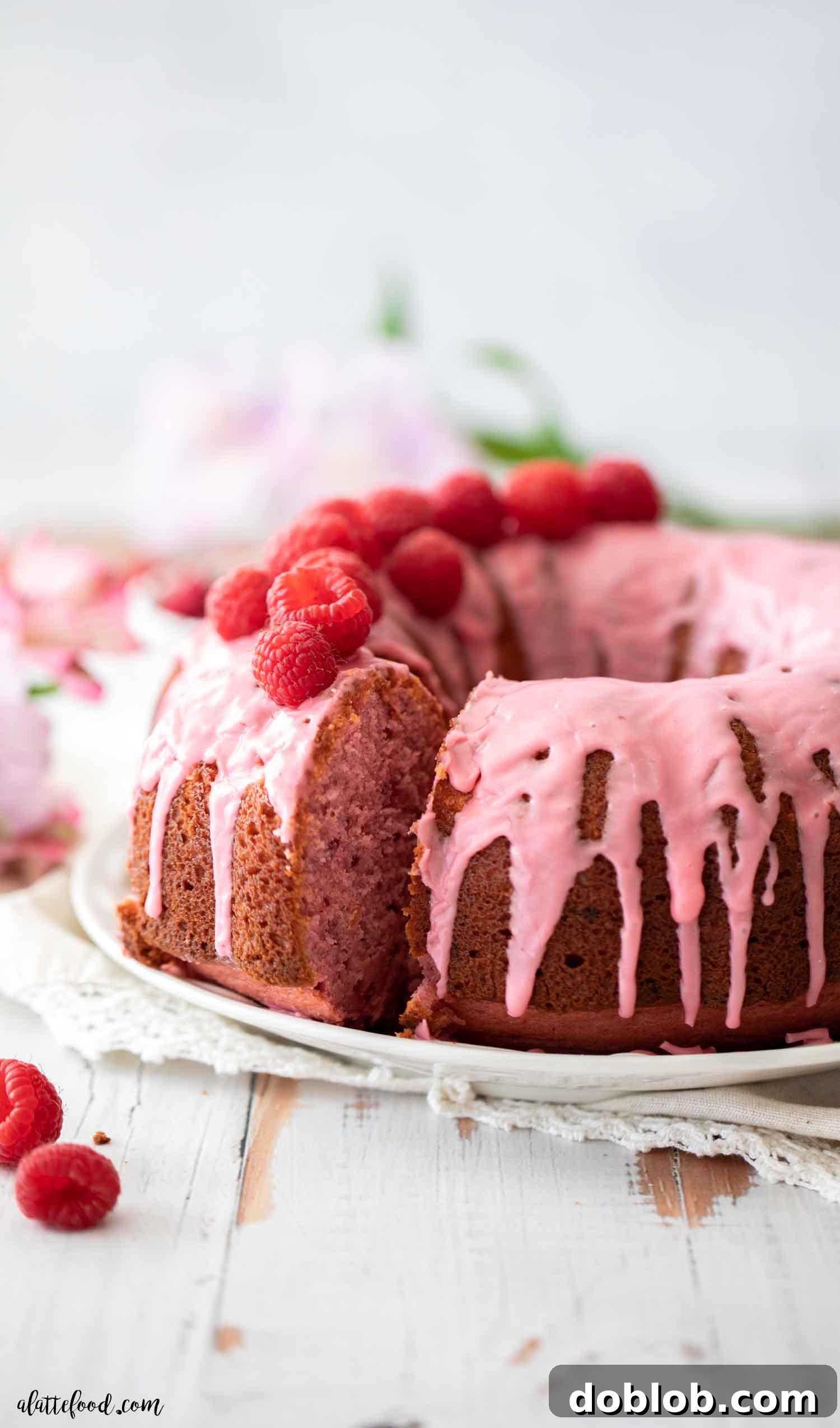 Making a Raspberry Bundt Cake from scratch is simple. This raspberry cake uses fresh ingredients, without gelatin or cake mix, relying on a fresh raspberry sauce and freeze-dried raspberries. It's an easy Valentine’s Day dessert and a delightful treat all year long. A beautiful slice of raspberry bundt cake, adorned with fresh raspberries, showcasing its moist, pink crumb and inviting texture.