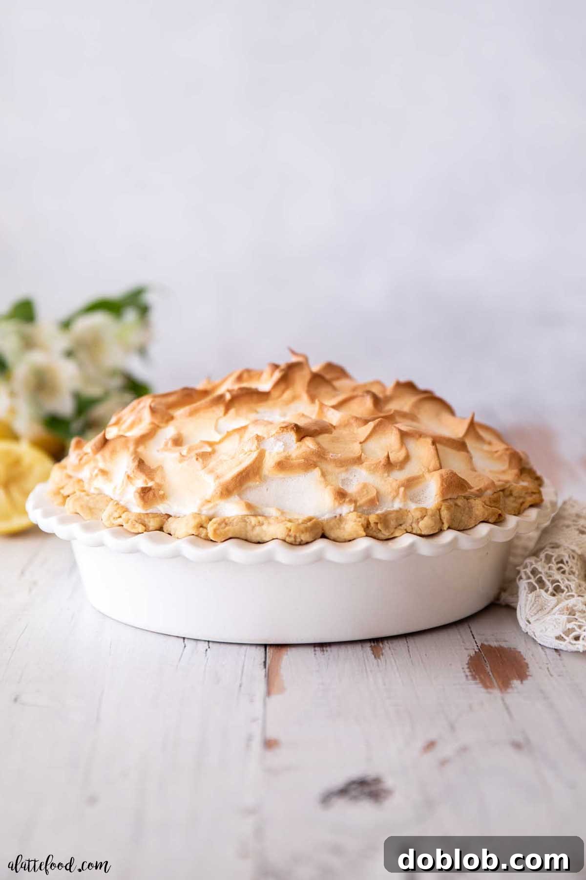 Whole lemon meringue pie with perfectly toasted meringue peaks in a white ceramic pie dish.