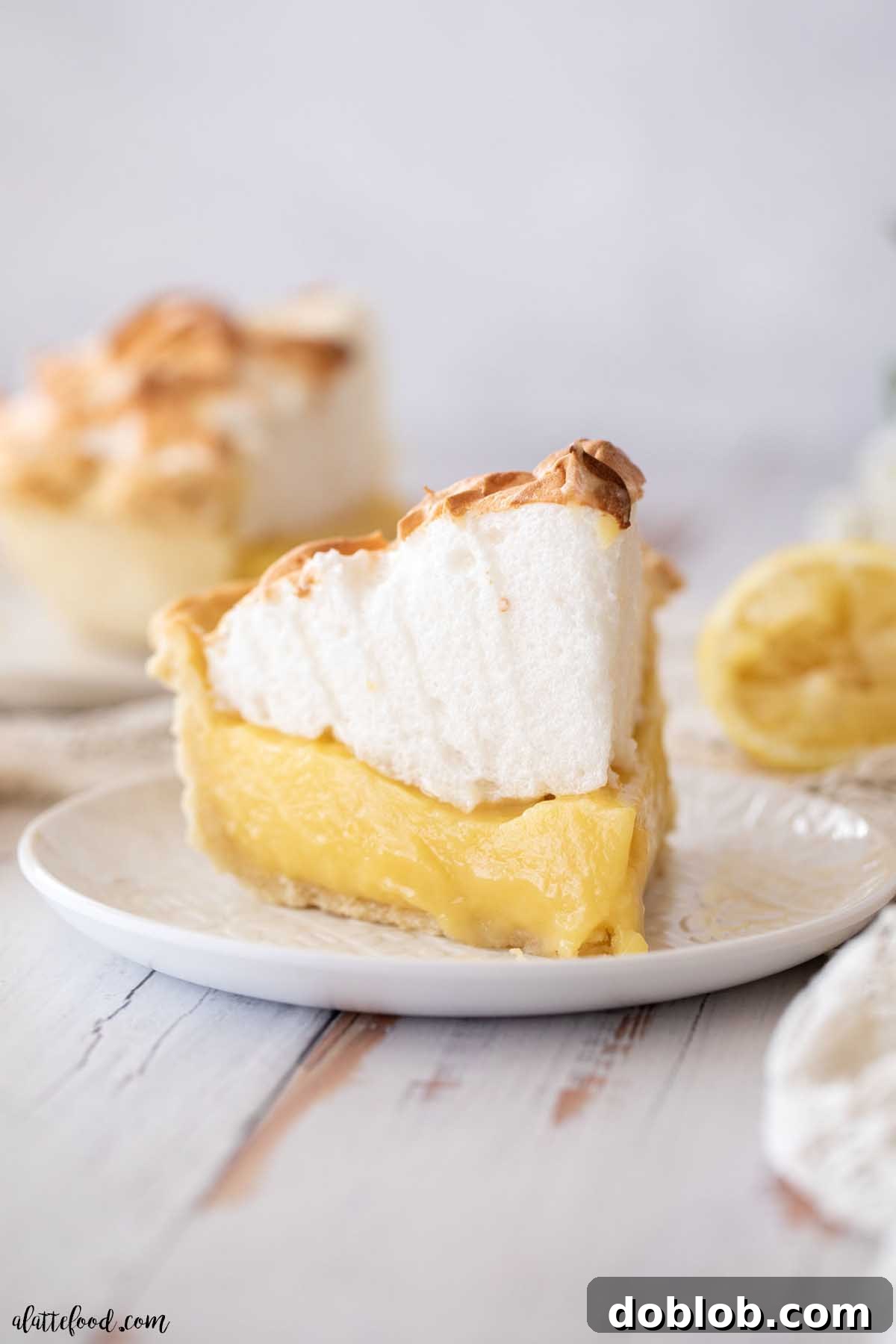 A perfectly sliced piece of homemade lemon meringue pie on a white plate, highlighting its creamy filling and tall meringue.