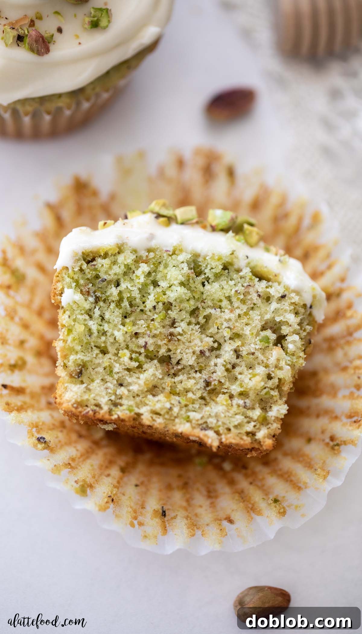 Light, fluffy, and made with real pistachios, these Honey Pistachio Cupcakes feature a vanilla cake base with almond and honey to enhance the natural pistachio flavor. Made entirely from scratch, no pudding mix needed! Fluffy pistachio cupcake cut in half revealing moist crumb