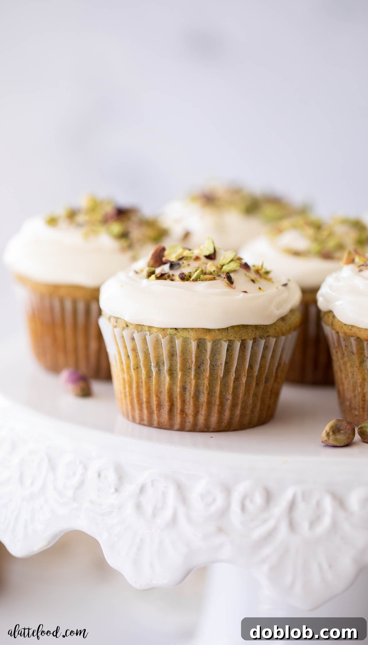 These homemade Honey Pistachio Cupcakes, topped with honey cream cheese frosting, are the perfect spring dessert. Featuring almond extract, honey, and real pistachios for a buttery, velvet texture. Honey pistachio cupcakes with cream cheese frosting on a cake stand