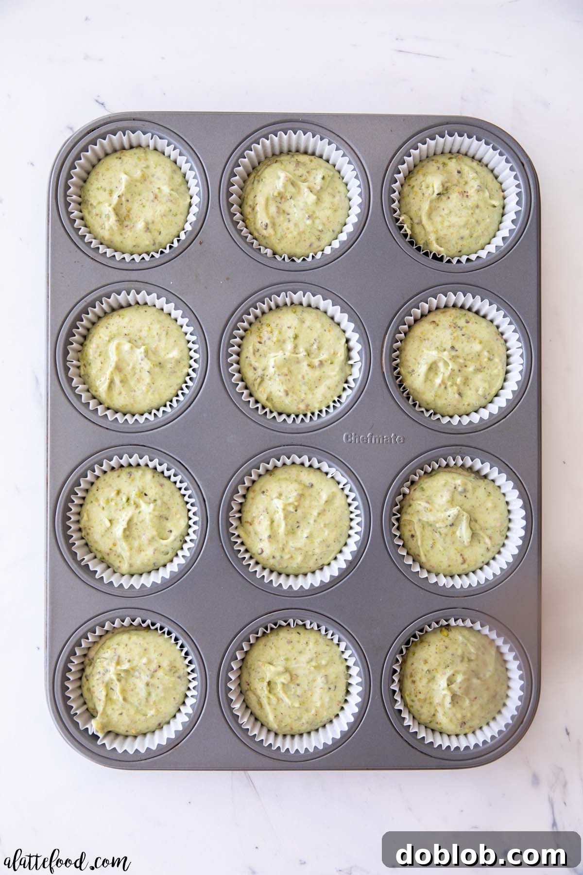 These scratch-made Honey Pistachio Cupcakes with Cream Cheese Frosting feature a vanilla cake with real pistachios, honey, and almond extract, offering a delicious alternative to pudding mix. Pistachio cupcake batter in muffin tins