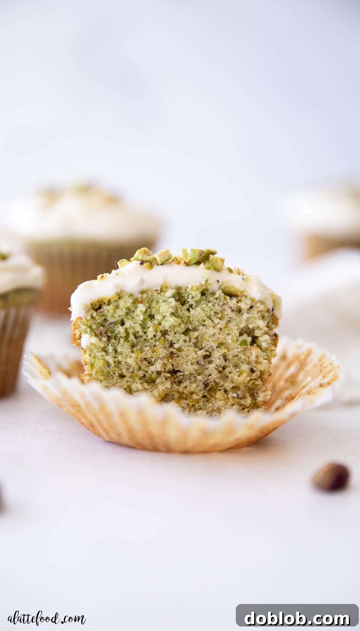 Ultra light and fluffy Homemade Pistachio Cupcakes with honey and almond extract. Made from scratch with fresh pistachios in a vanilla cupcake base, topped with honey cream cheese frosting. Cream cheese frosted pistachio honey cupcake cut in half
