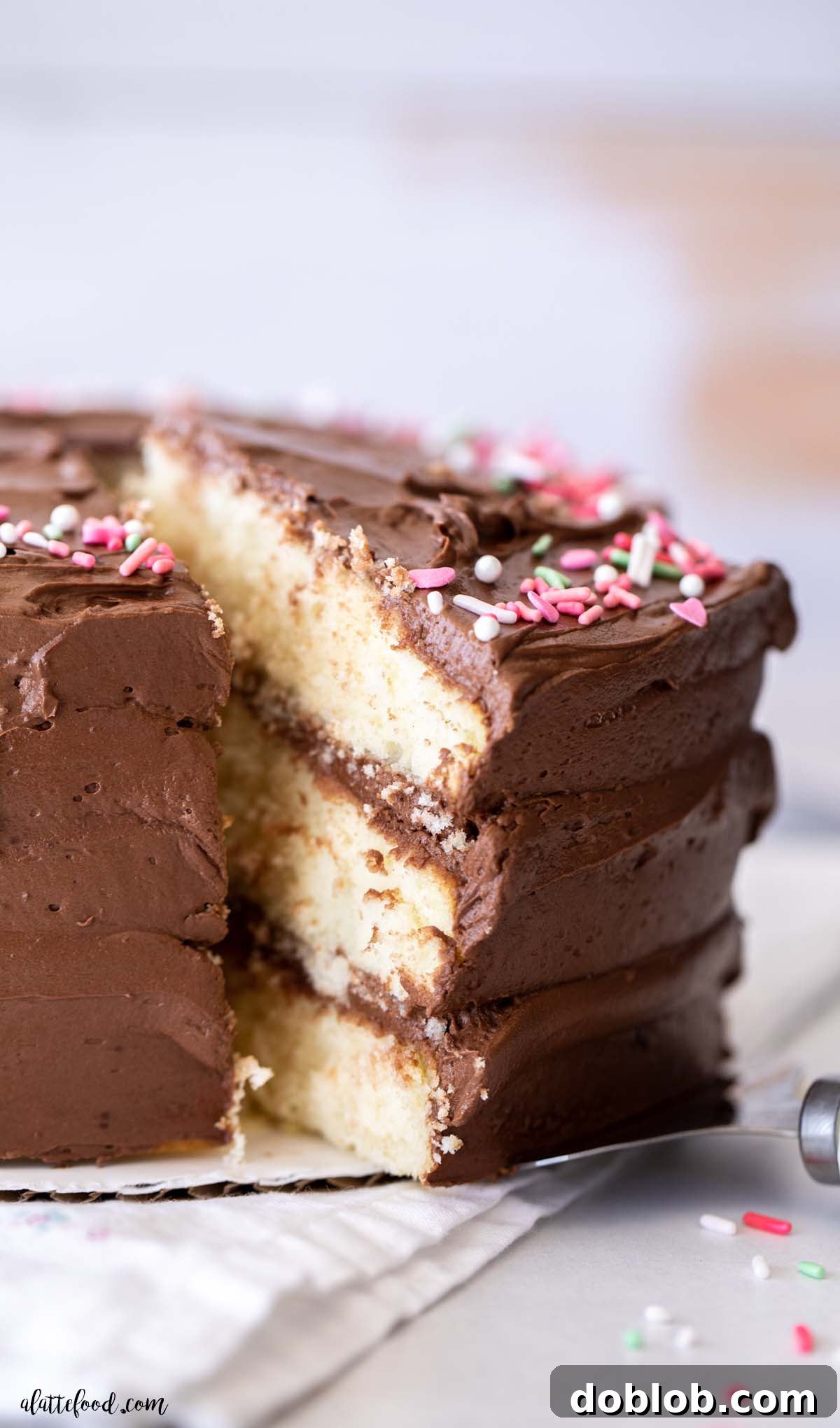 A delectable slice of triple-layer yellow cake, generously frosted with rich chocolate buttercream and adorned with colorful sprinkles, promising a perfect bite.