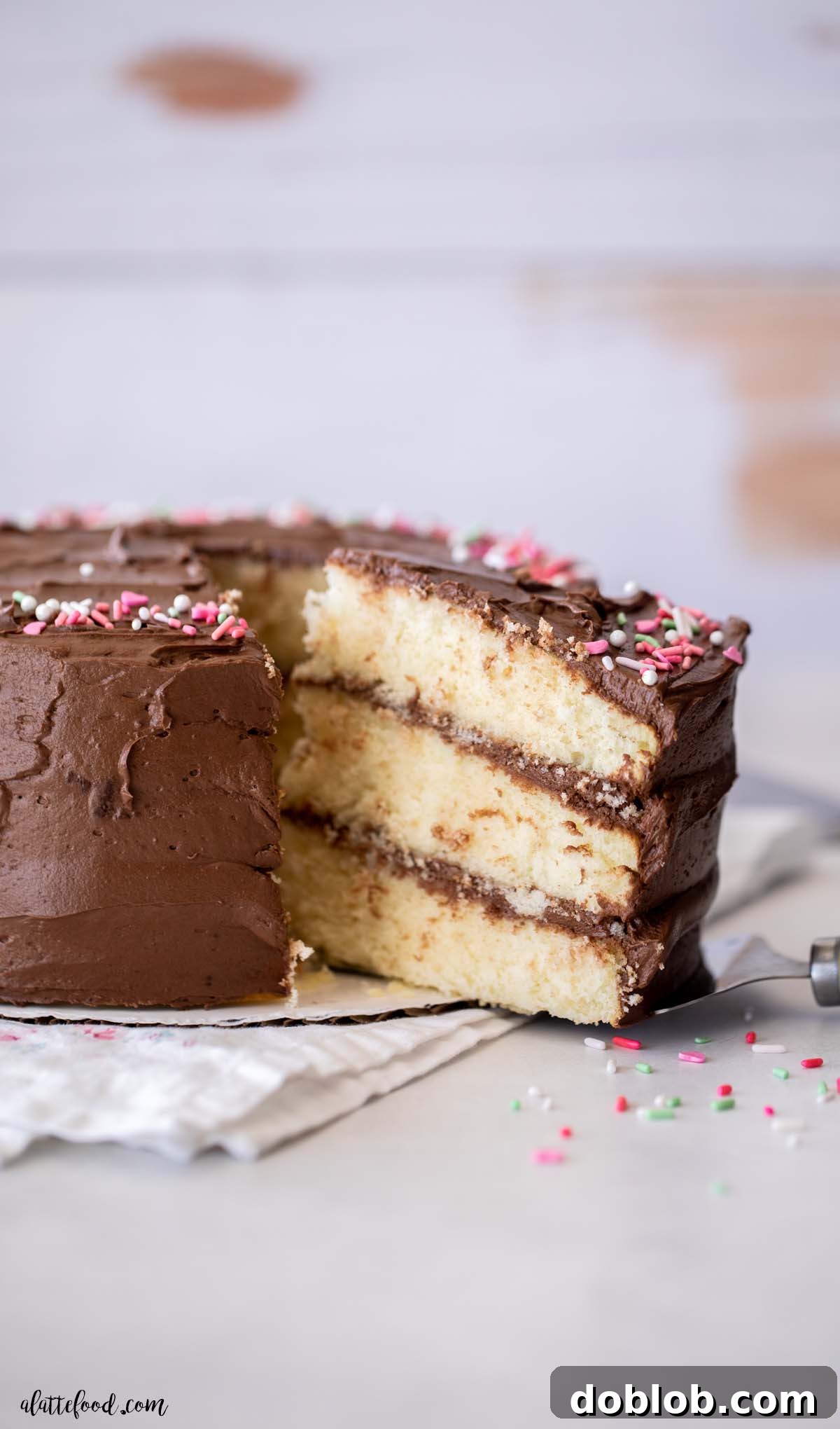 A generous slice of fluffy yellow cake with luxurious chocolate frosting, elegantly served on a cake server, highlighting its tender crumb.
