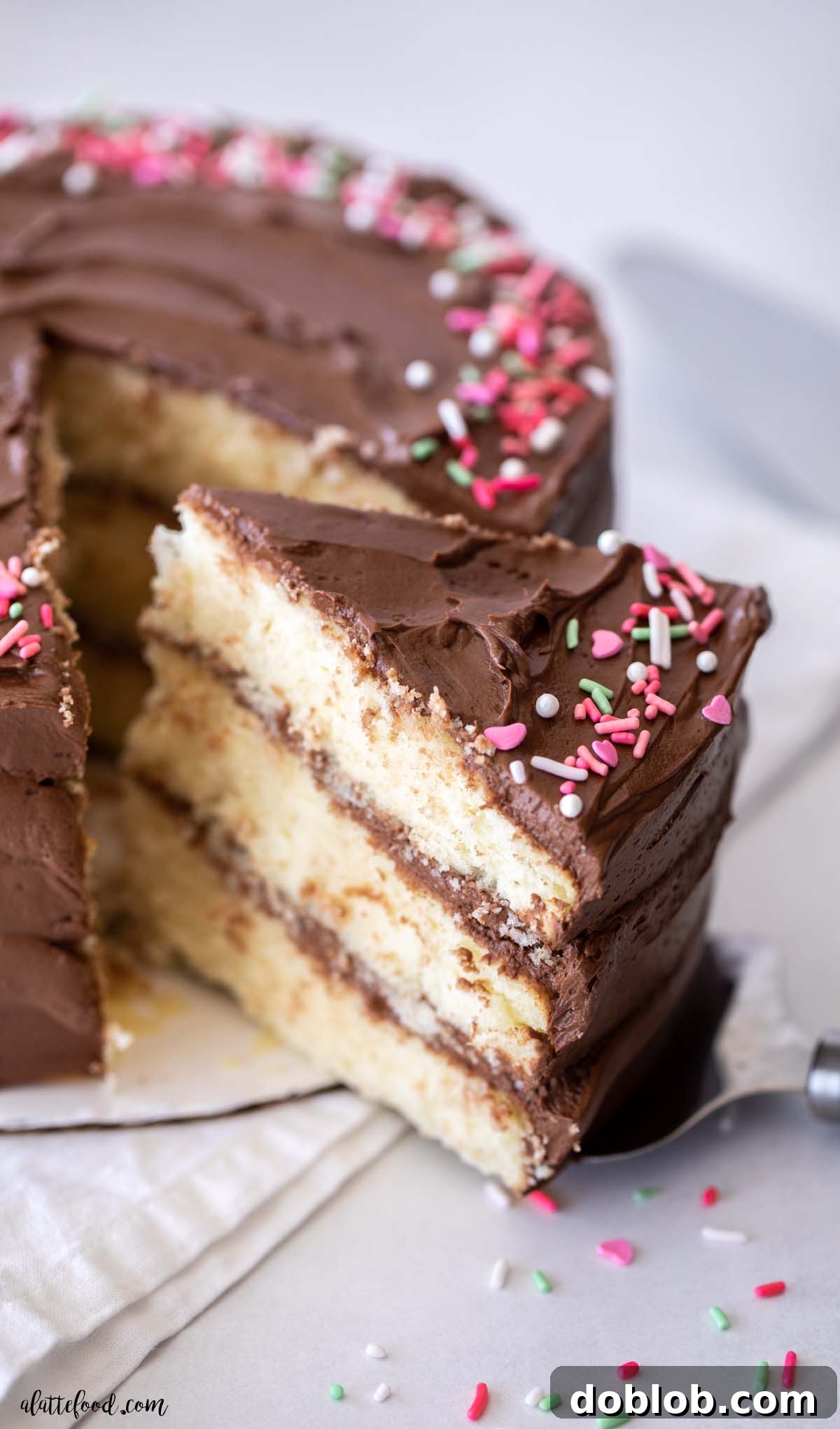 A perfectly sliced piece of yellow cake, revealing its moist crumb and topped with a generous swirl of chocolate frosting on a cake server.