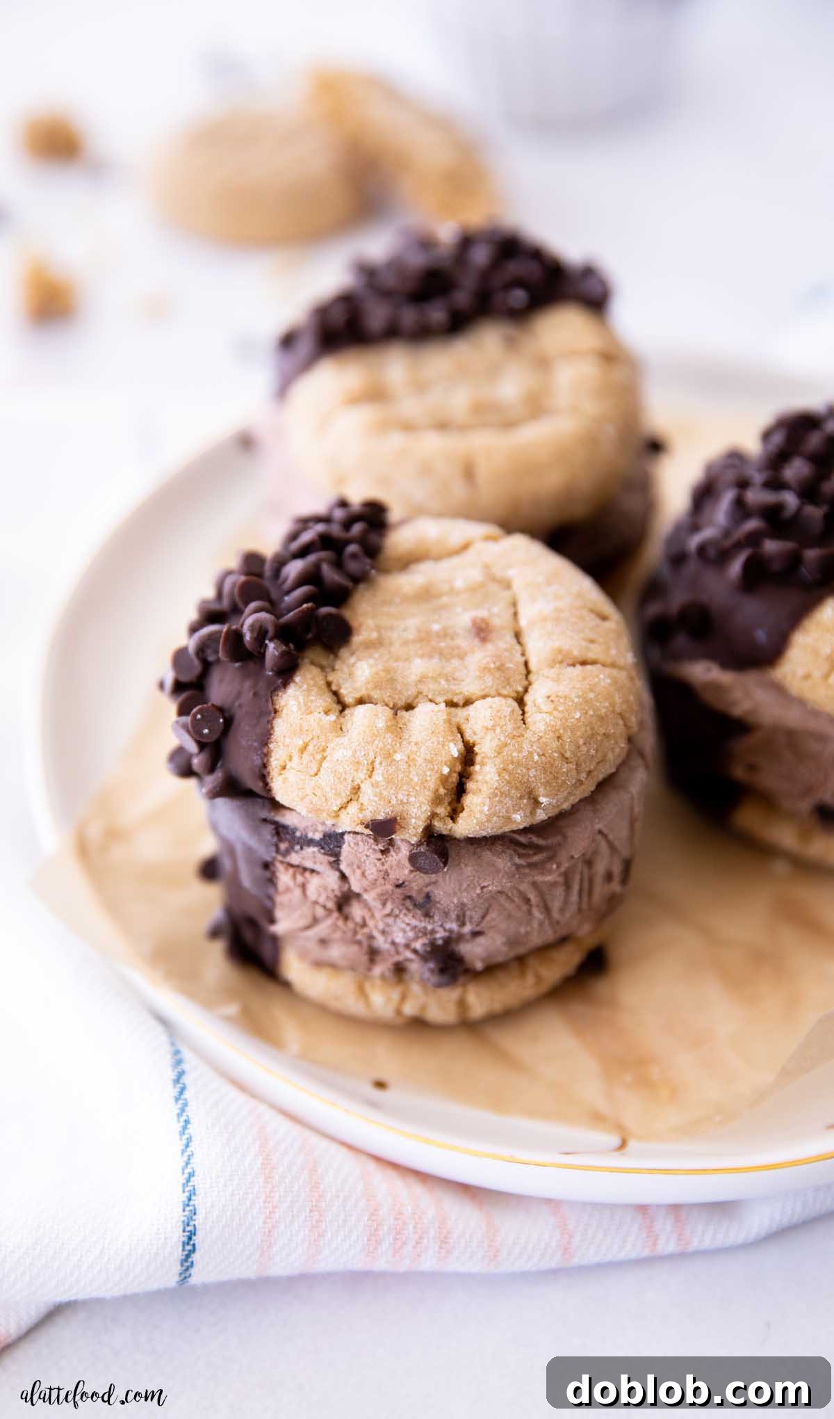 Three chocolate peanut butter cookie ice cream sandwiches dipped in magic shell, arranged on parchment paper on a white plate