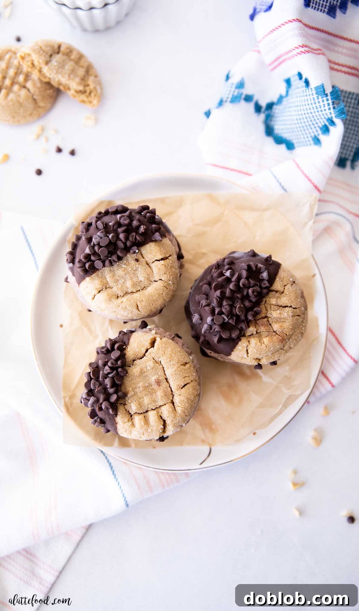 Three chocolate-dipped peanut butter ice cream sandwiches on a white plate, ready to be enjoyed