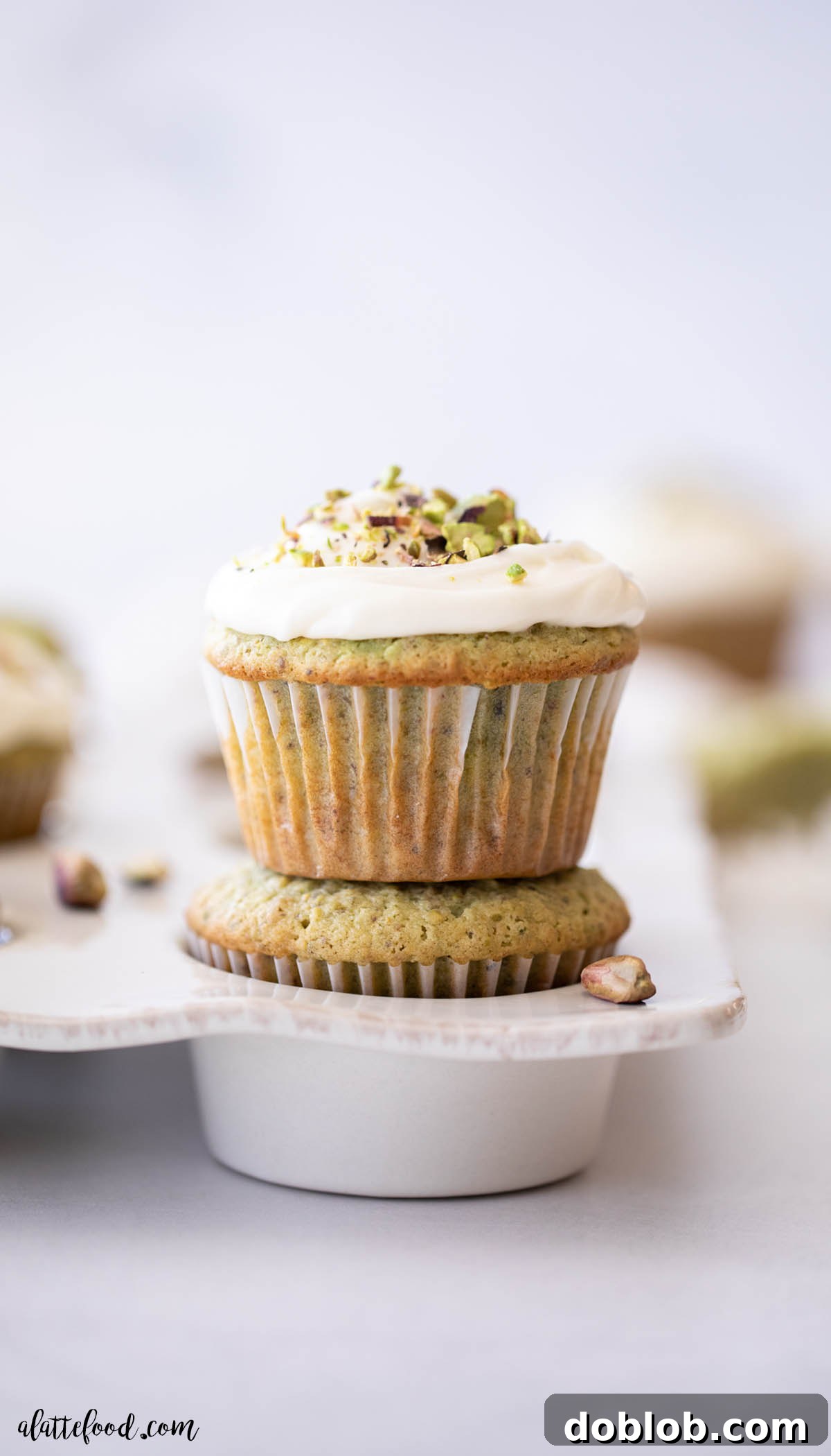 Honey Pistachio Cupcakes with Cream Cheese Frosting stacked on top of each other in a white muffin tin, showcasing their delightful green hue.