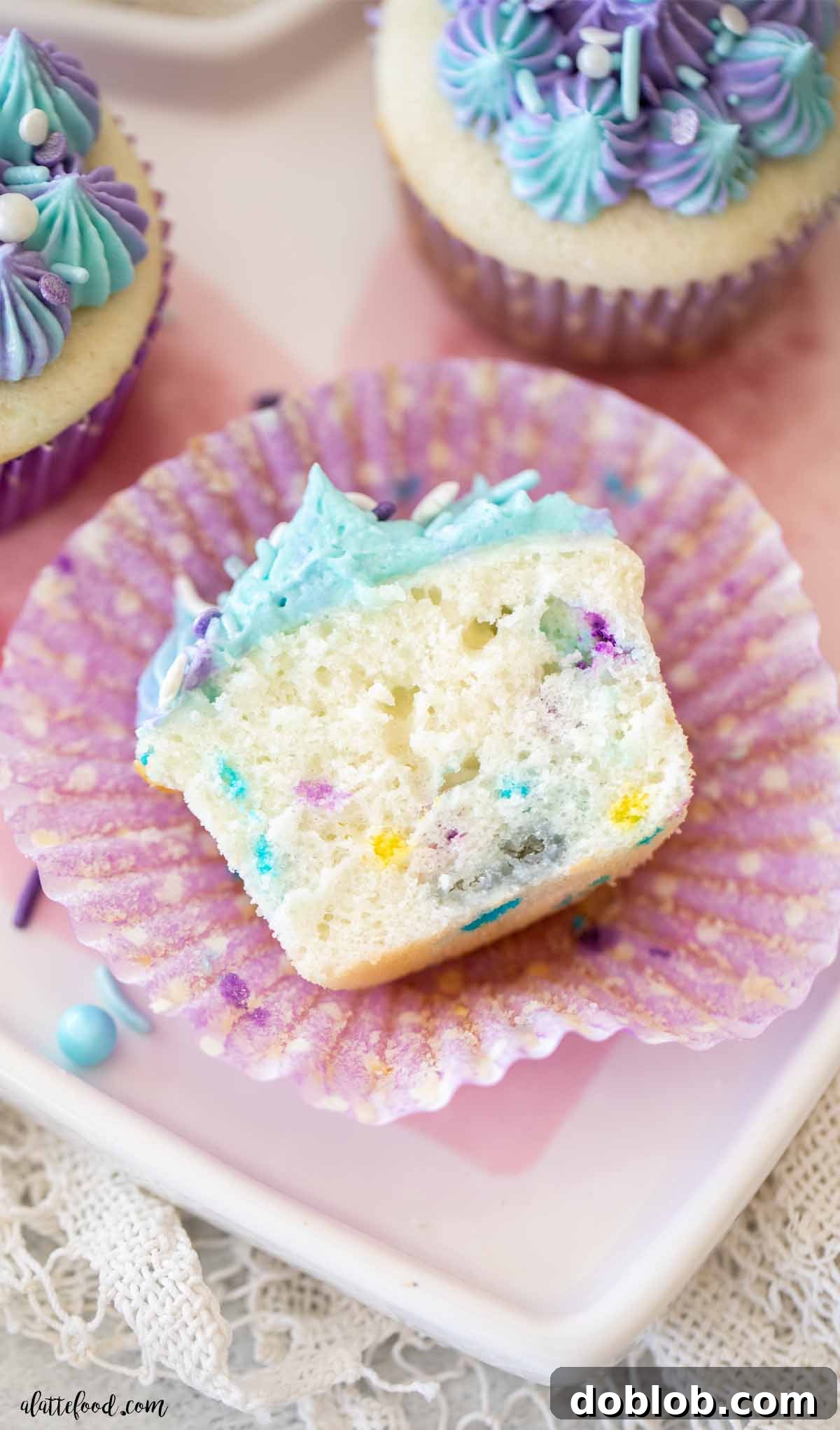 A perfectly baked Funfetti cupcake, cut in half to reveal its moist, sprinkle-filled interior, nestled in a vibrant purple polka-dot cupcake liner.
