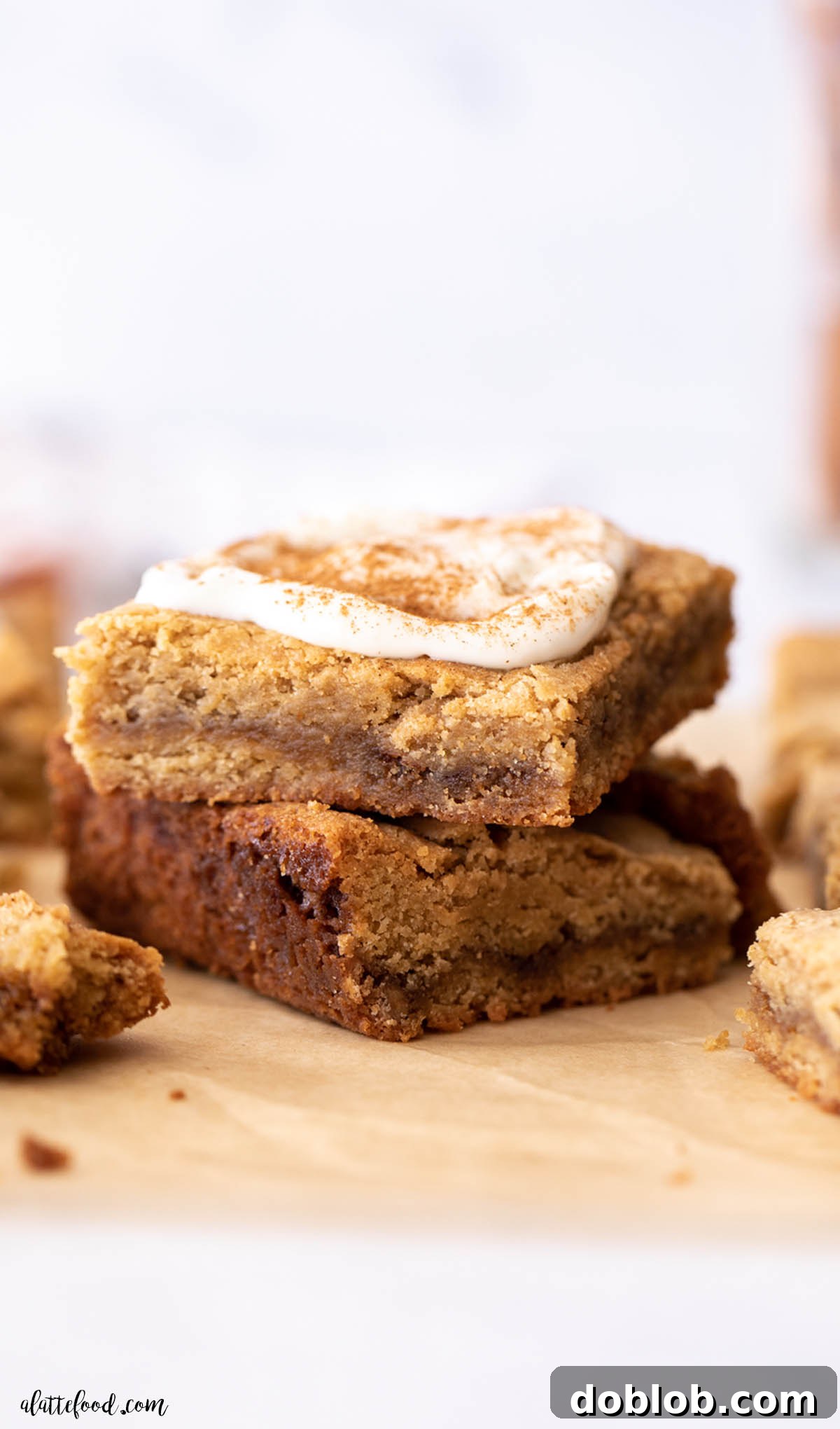 two cinnamon roll blondies with cream cheese frosting stacked on brown parchment paper