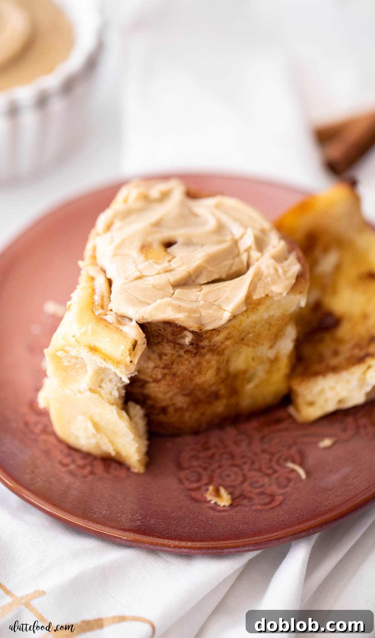 gooey cinnamon roll with pumpkin butter and brown sugar frosting on red plate