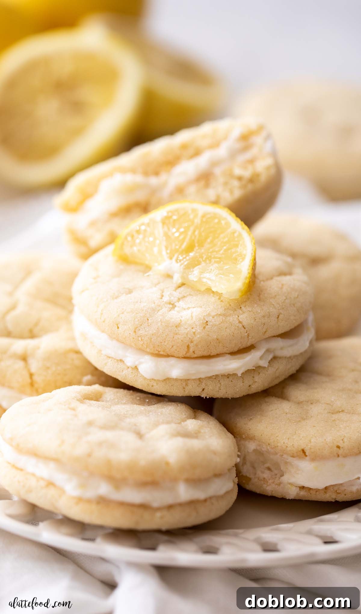 soft lemon sandwich cookies filled with lemon frosting on a white plate with fresh lemon wedges
