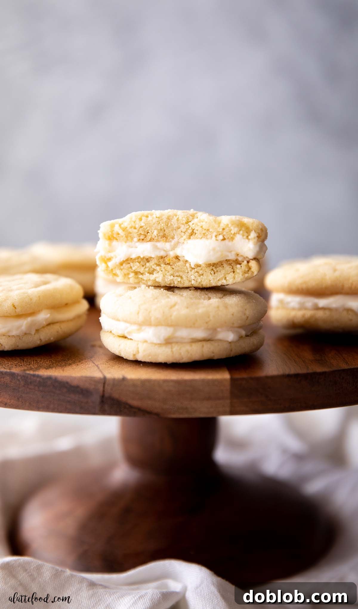 Soft Lemon Sandwich Cookie cut in half with lemon frosting oozing out of the center, sitting atop a wooden cake stand