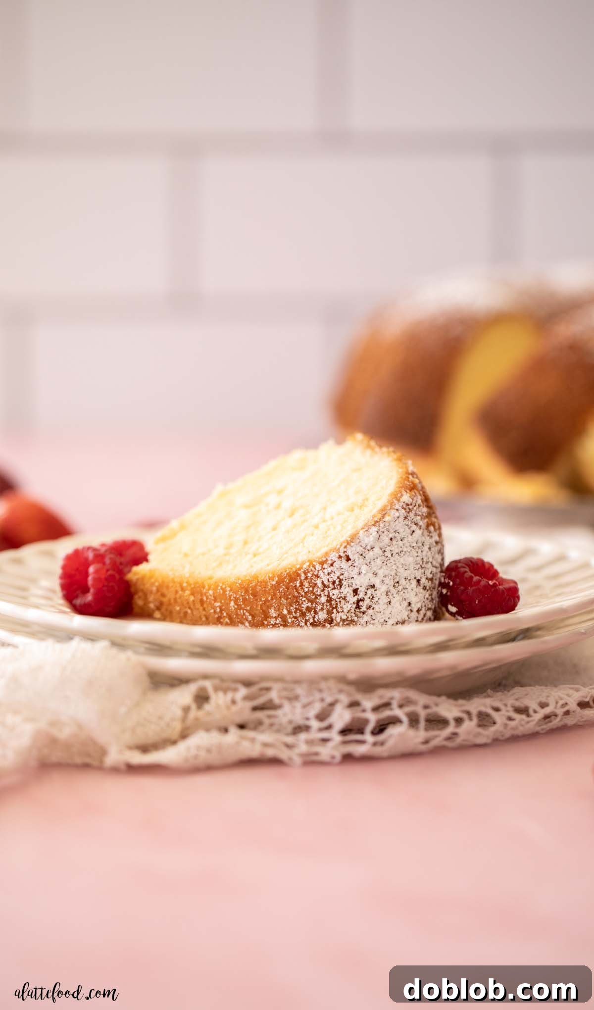 A single slice of moist cream cheese pound cake adorned with fresh raspberries, presented on a pristine white plate, highlighting its tender crumb.