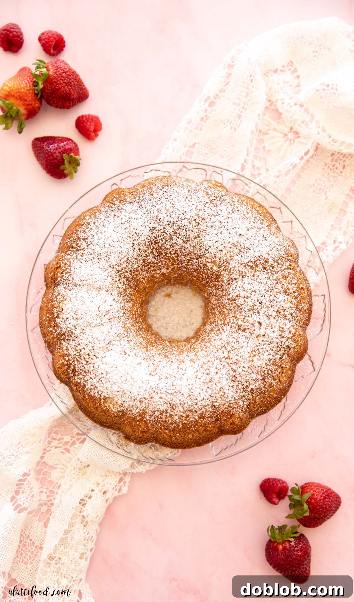 A beautifully decorated cream cheese pound cake slice, topped with a generous assortment of fresh strawberries and raspberries, sitting on a clear glass plate.