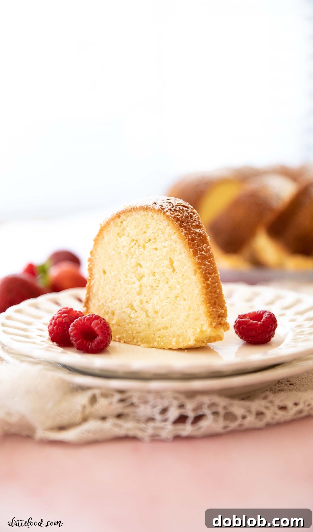 A pristine slice of homemade pound cake, enriched with cream cheese, beautifully presented with fresh raspberries on a white fluted plate.