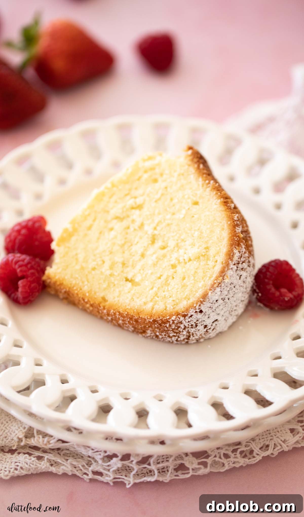 A single, delectable slice of cream cheese pound cake, topped with vibrant fresh raspberries, elegantly placed on a white serving plate, showcasing its moist texture.