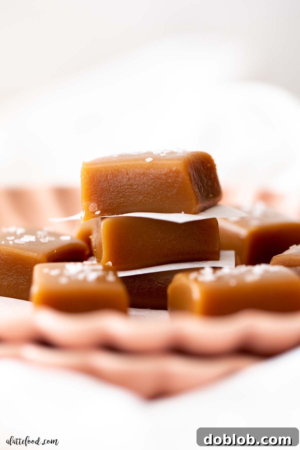 Caramel candies stacked on top of each other with parchment paper on a pink plate.