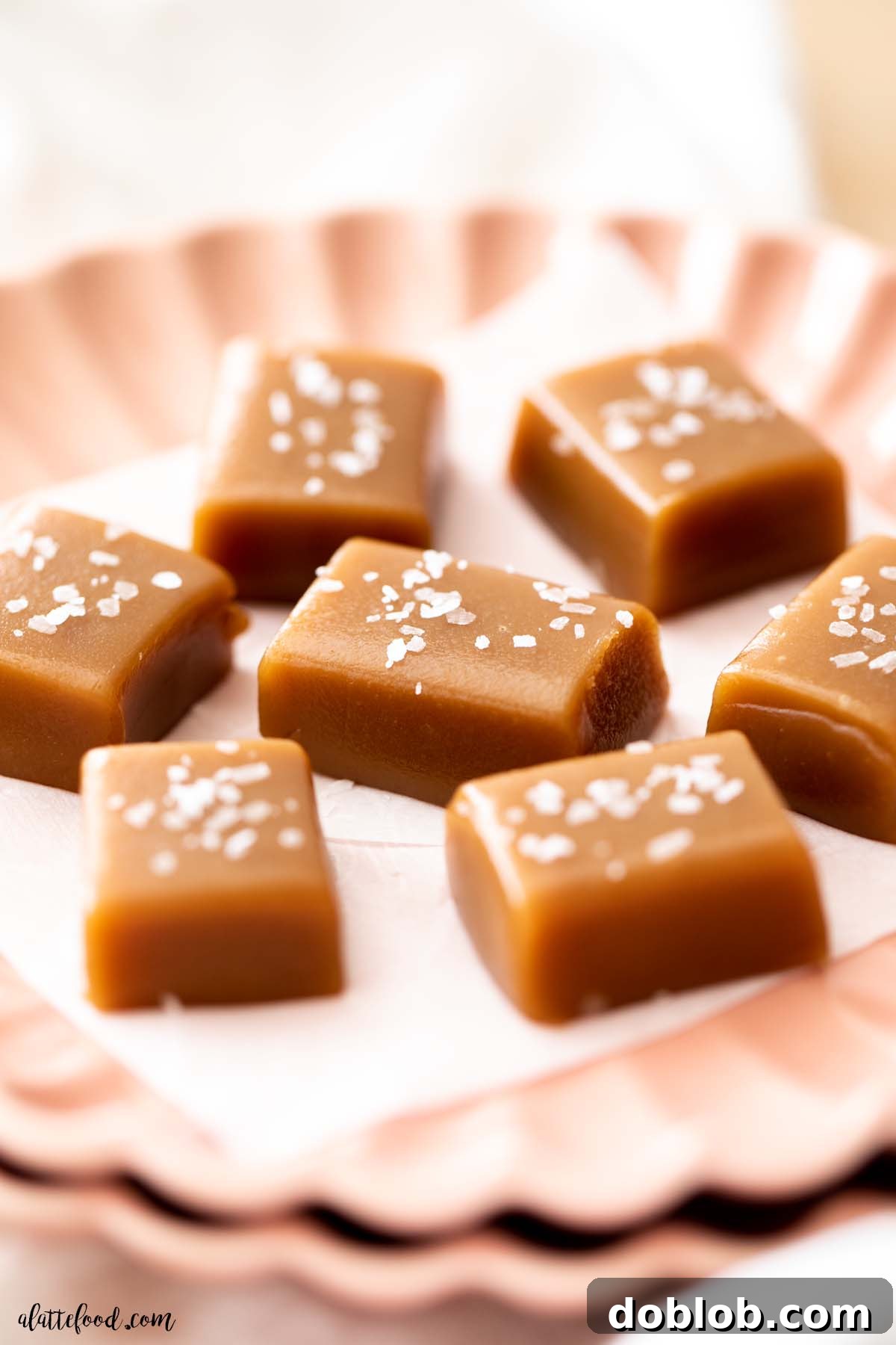 Easy microwave caramels with flaked sea salt cut into squares and served on a pink plate.