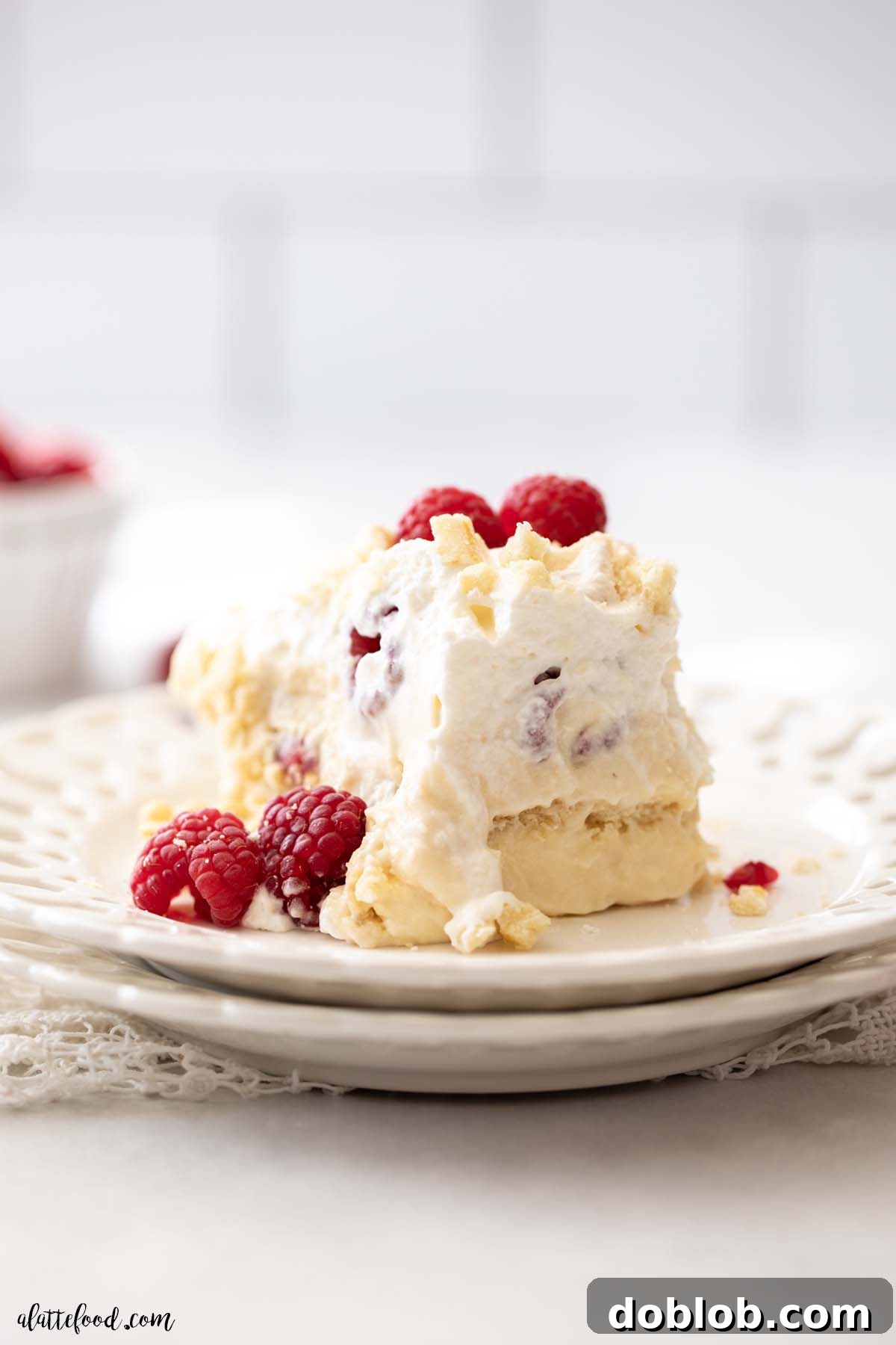Slice of White Chocolate Raspberry Pudding dessert with fresh raspberries on a white plate, showcasing beautiful layers.
