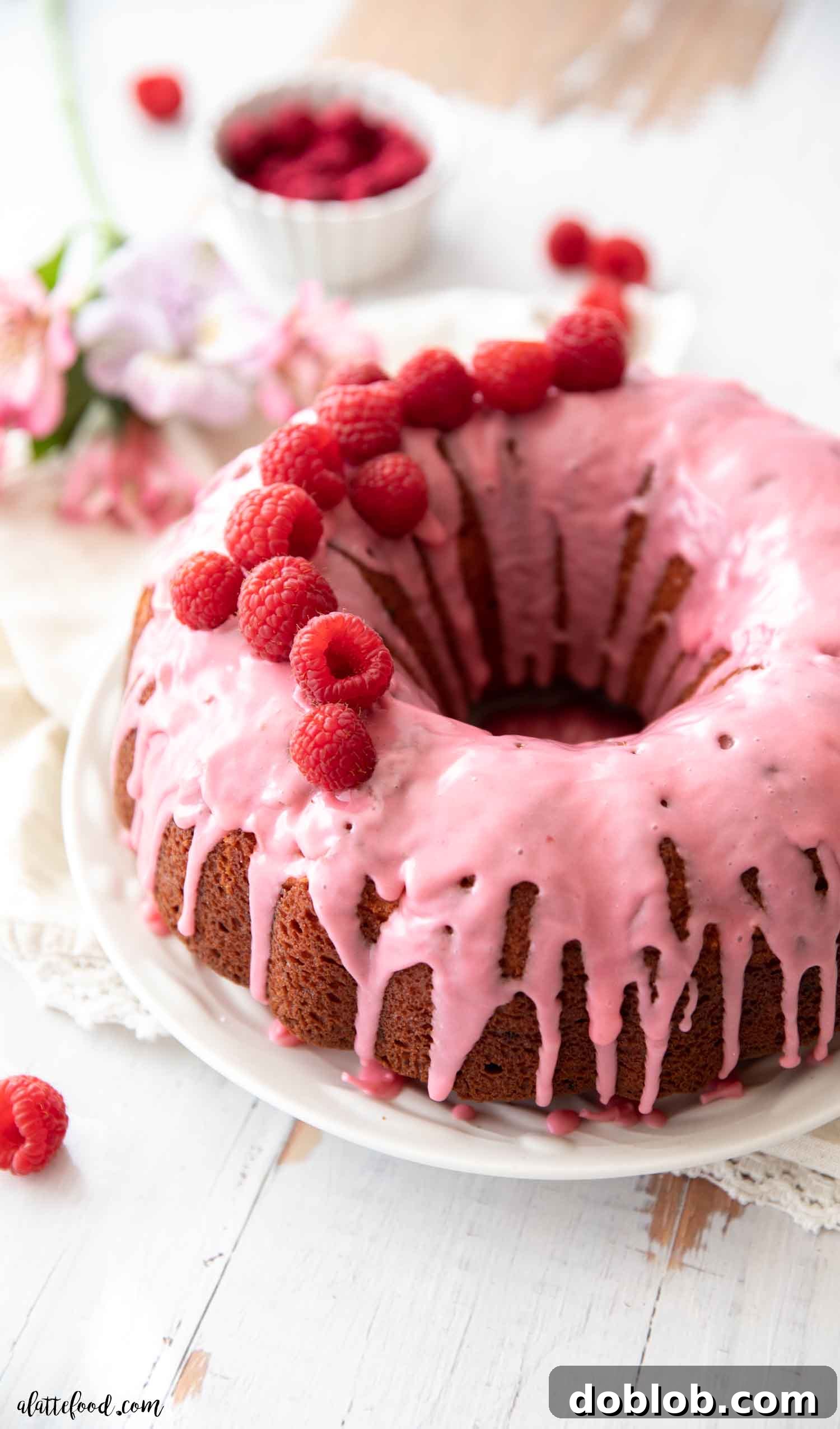 Raspberry Bundt Cake with fresh raspberries and pink raspberry glaze on a white plate, beautifully presented.